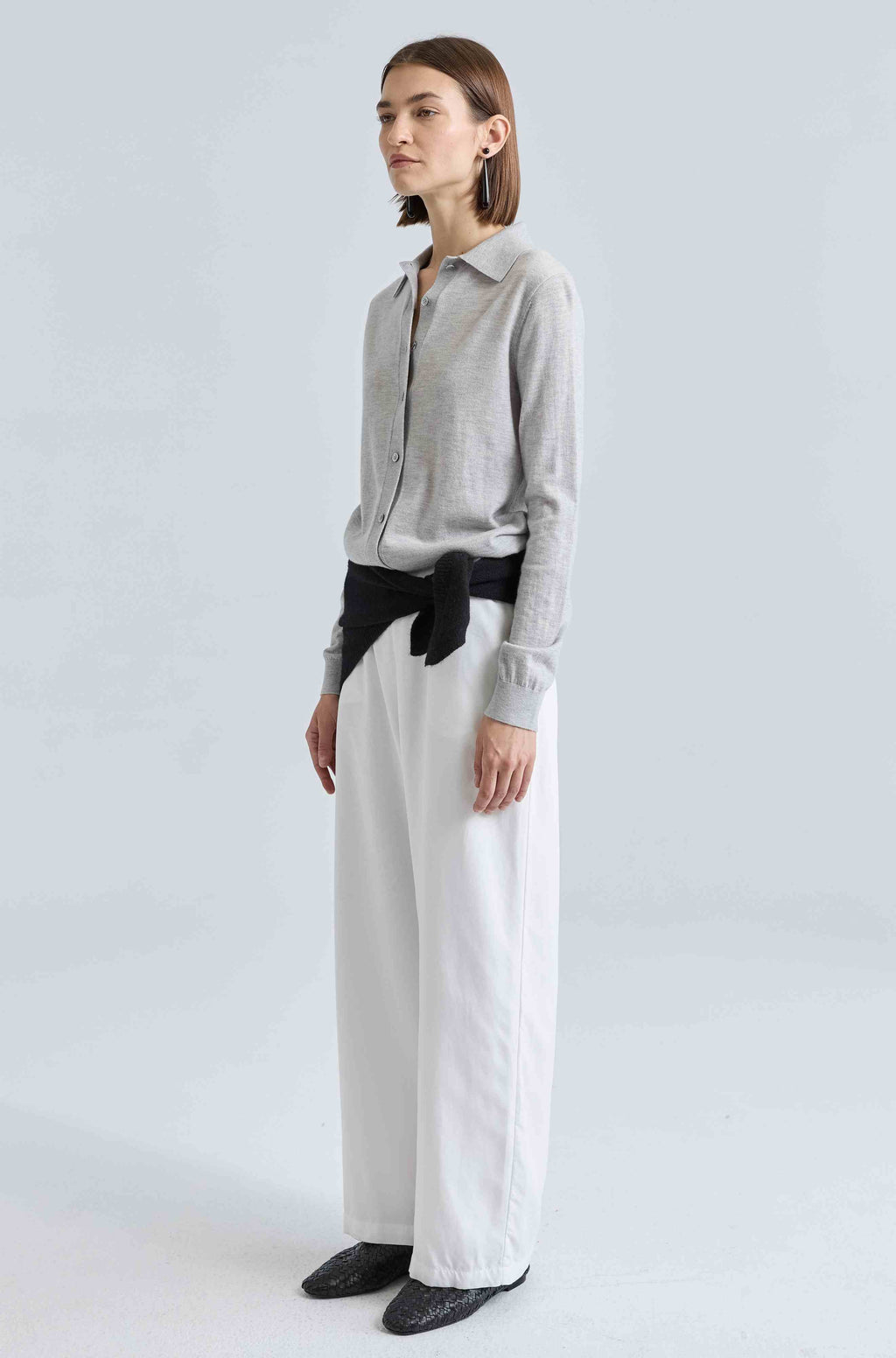 Woman wearing a gray shirt and white pants against a light gray background
