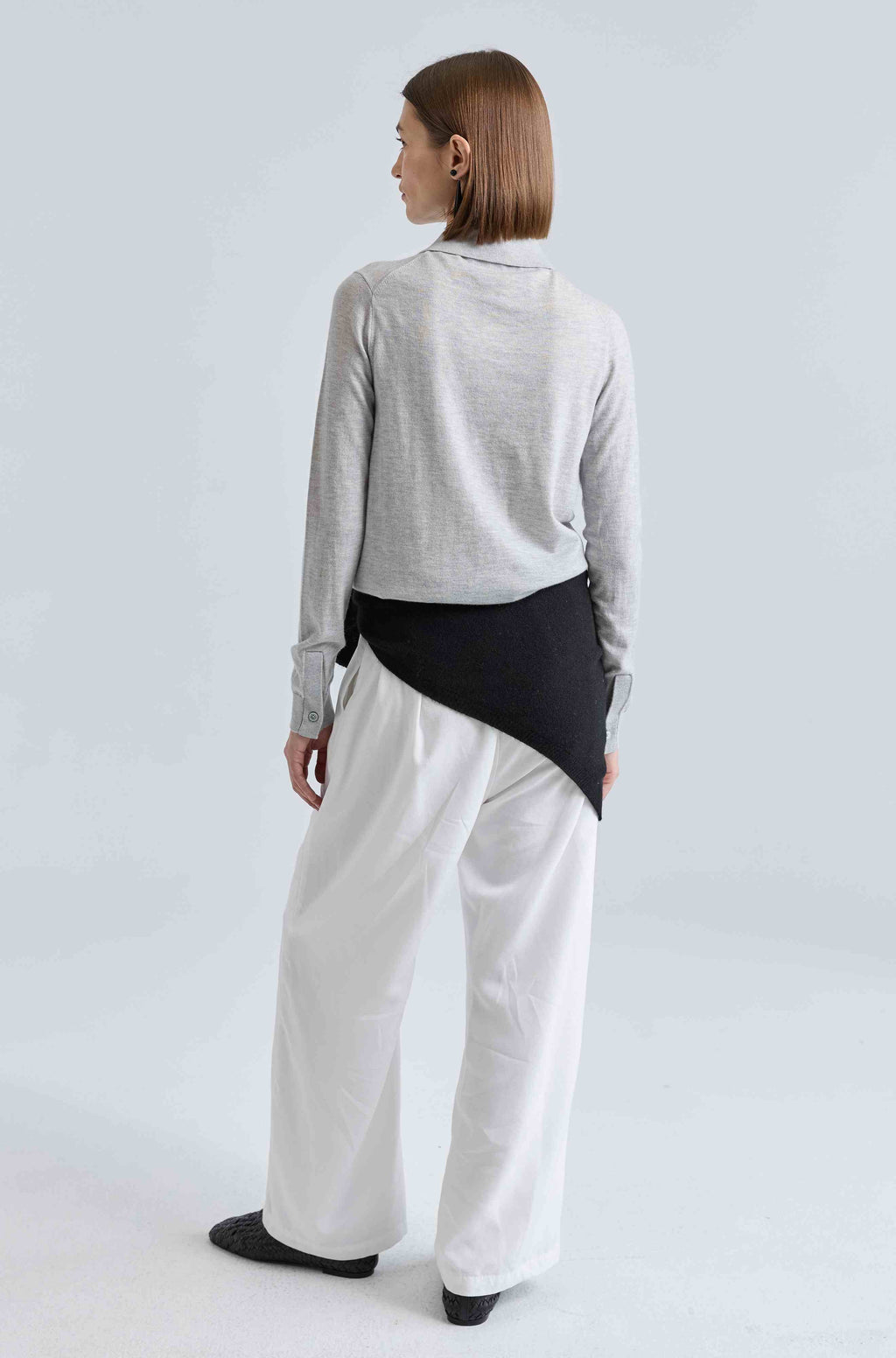 Person wearing a light gray long-sleeve top and white pants on a light gray background