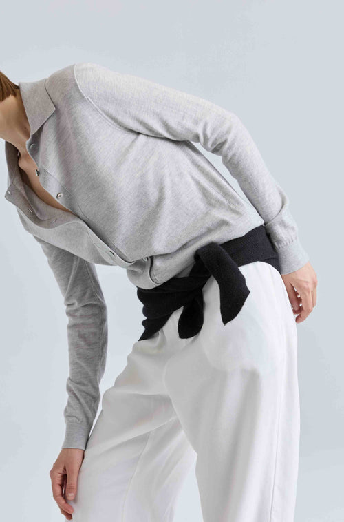 Person wearing a gray sweater, black belt, and white pants on a light blue background