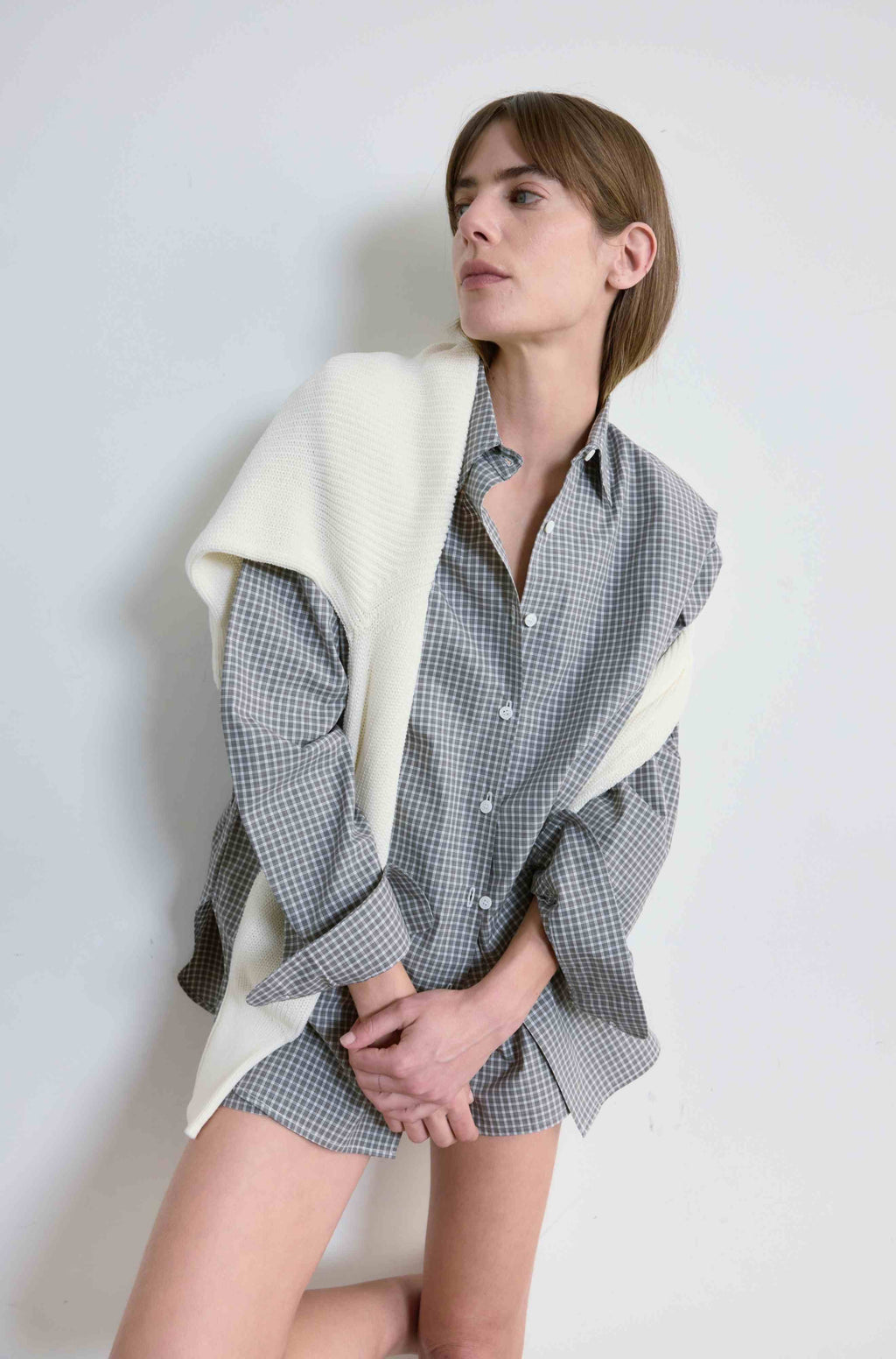 Woman wearing a checkered shirt and shorts with a white blanket draped over her shoulders against a plain background