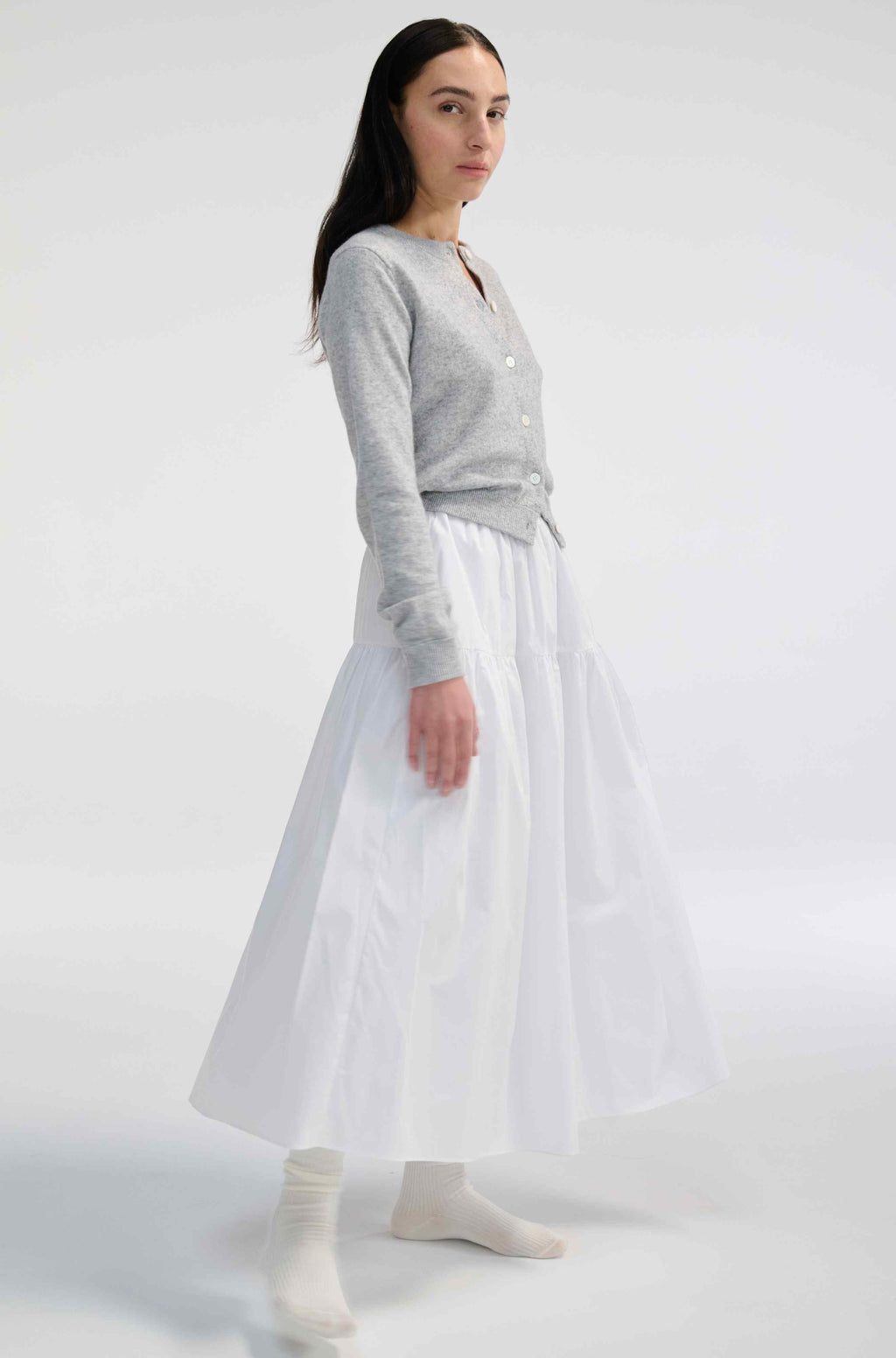 Woman wearing a gray sweater and white skirt on a white background