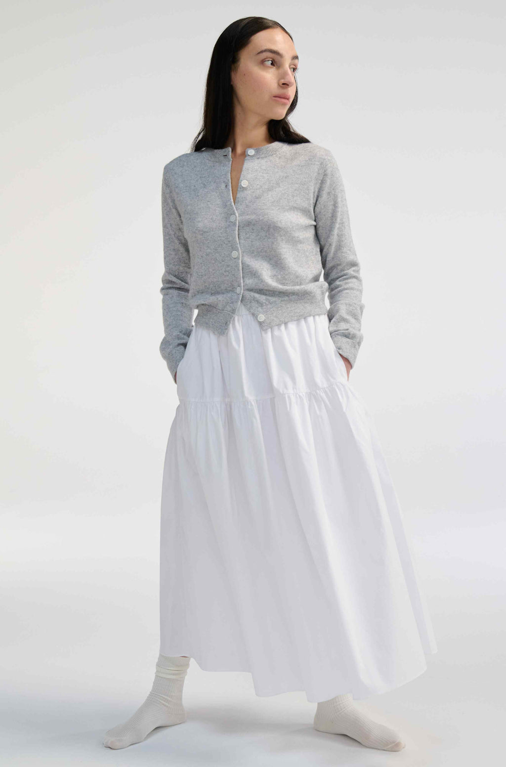 Woman wearing a gray cardigan and white skirt on a white background