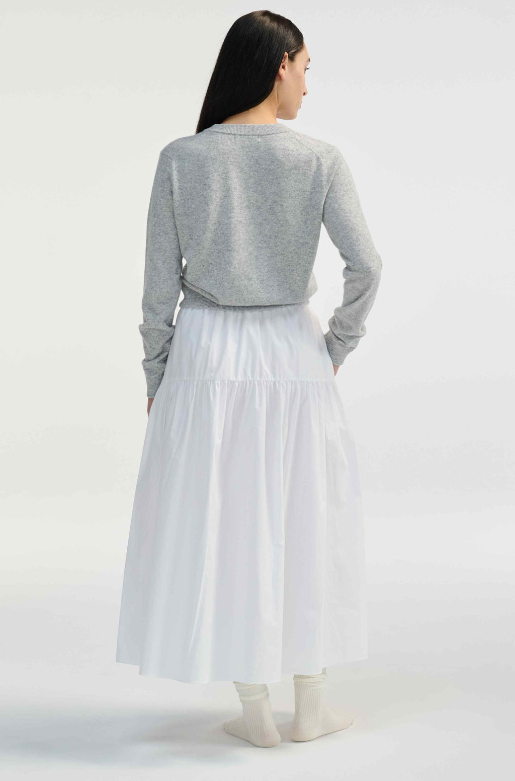 Woman wearing a gray cardigan over a white skirt on a white background