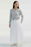 Woman wearing a gray cardigan and white midi skirt on a white background