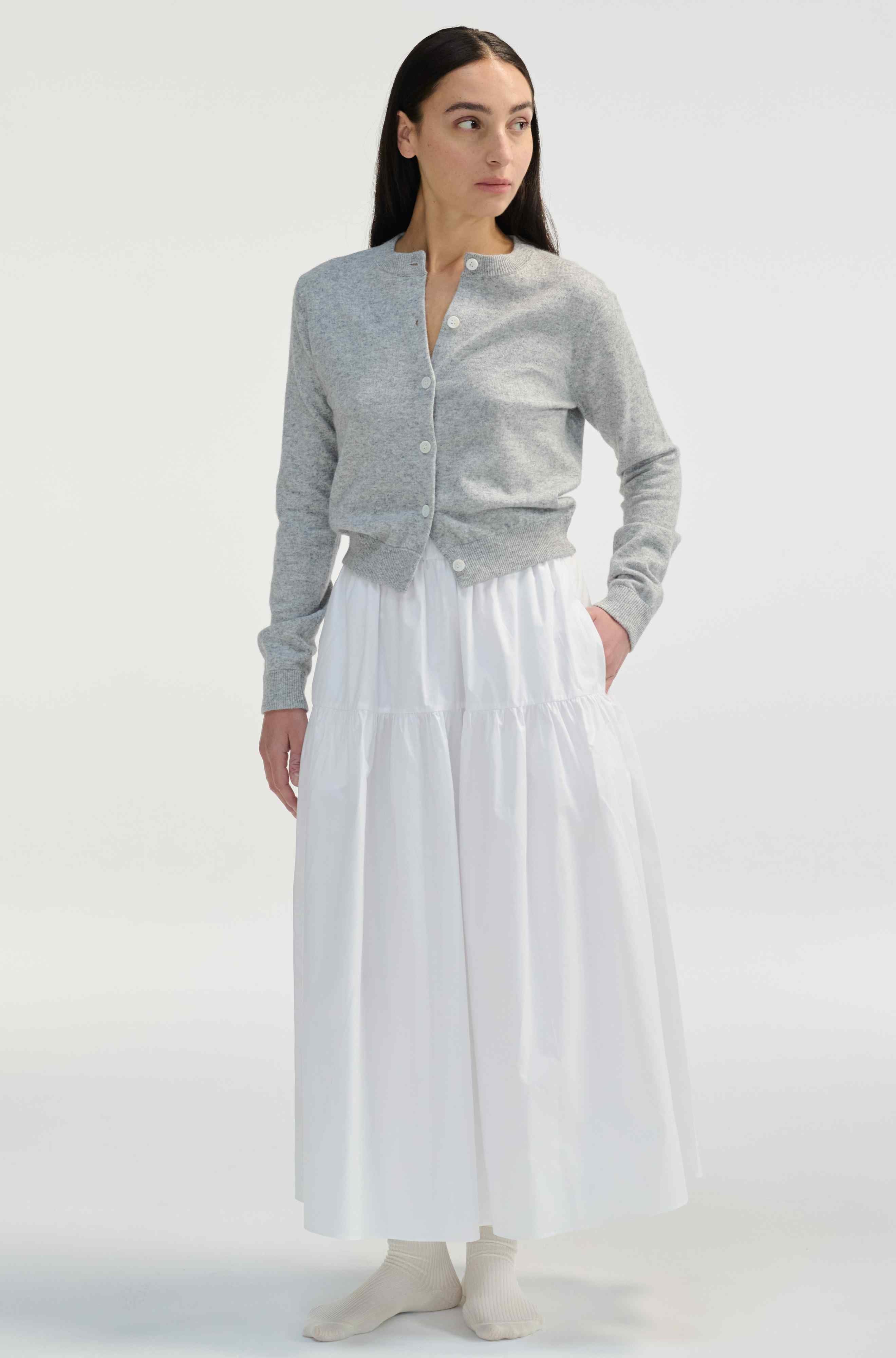 Woman wearing a gray cardigan and white midi skirt on a white background
