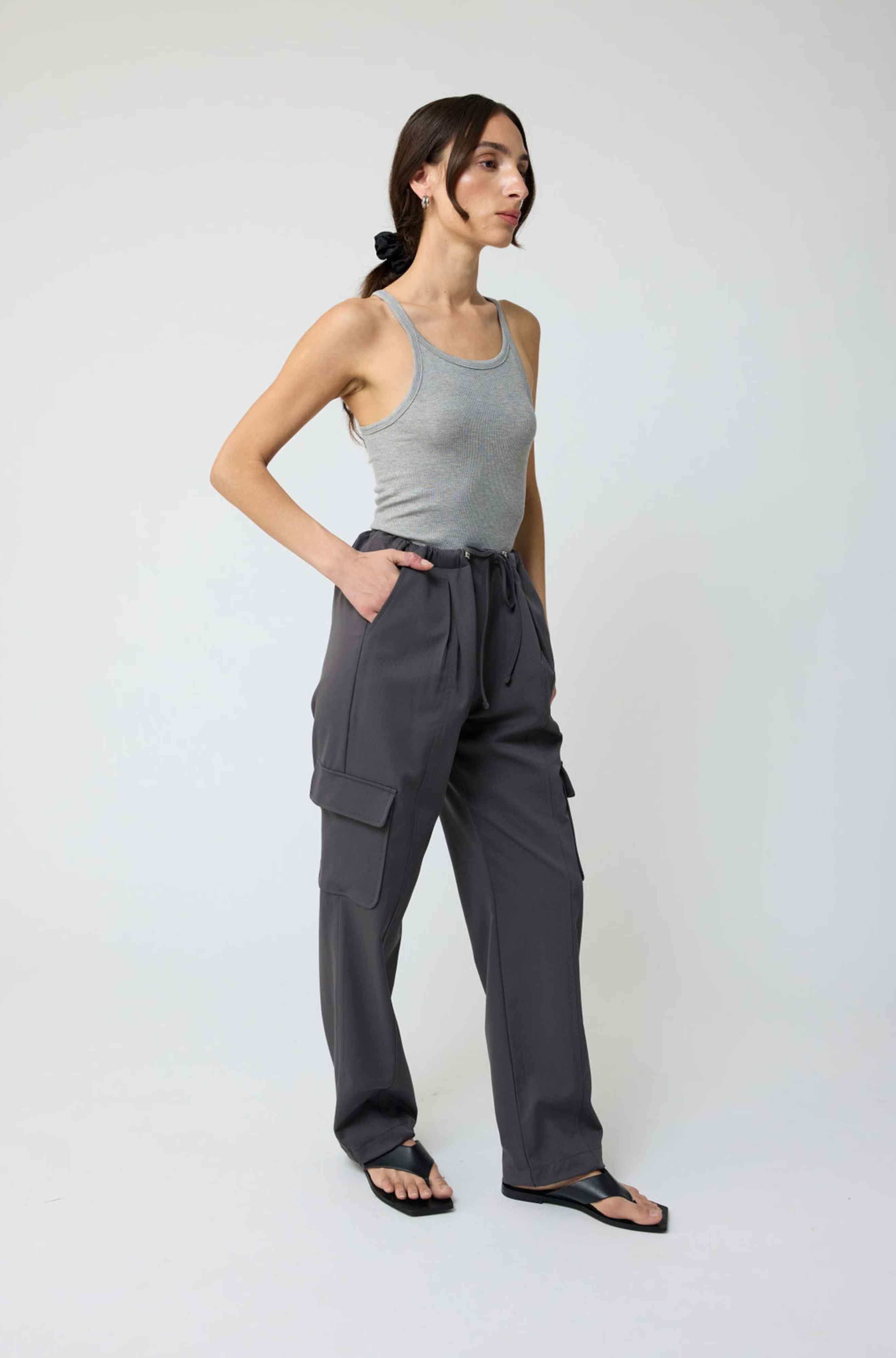 Woman wearing a gray tank top and dark gray cargo pants on a white background