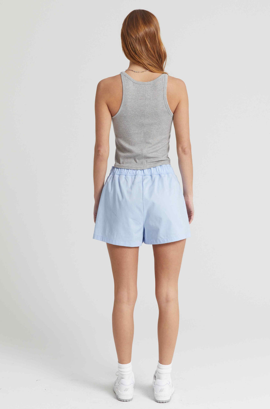 Person wearing a gray tank top and light blue shorts on a white background