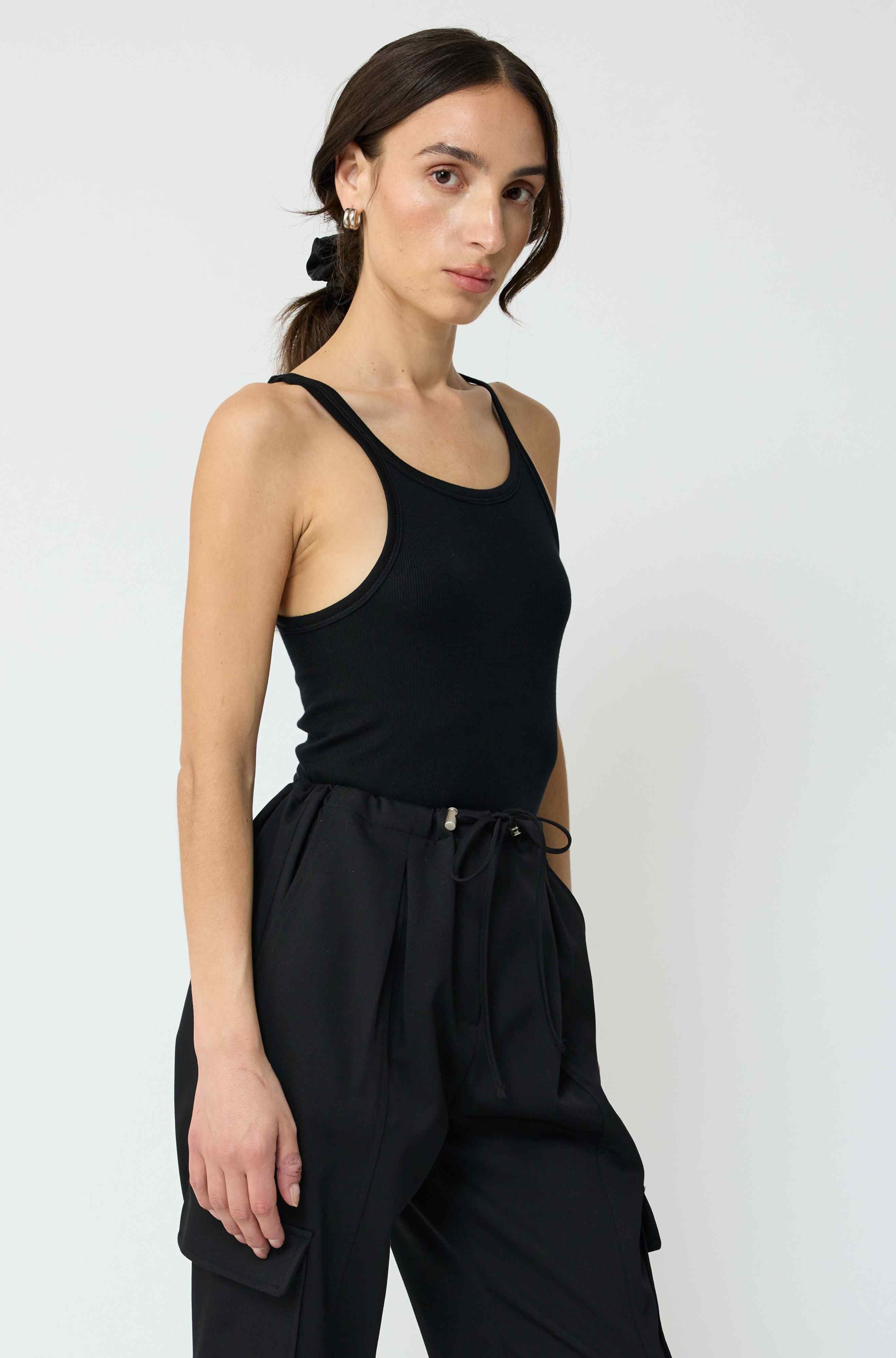 Woman wearing a black tank top and black pants against a white background