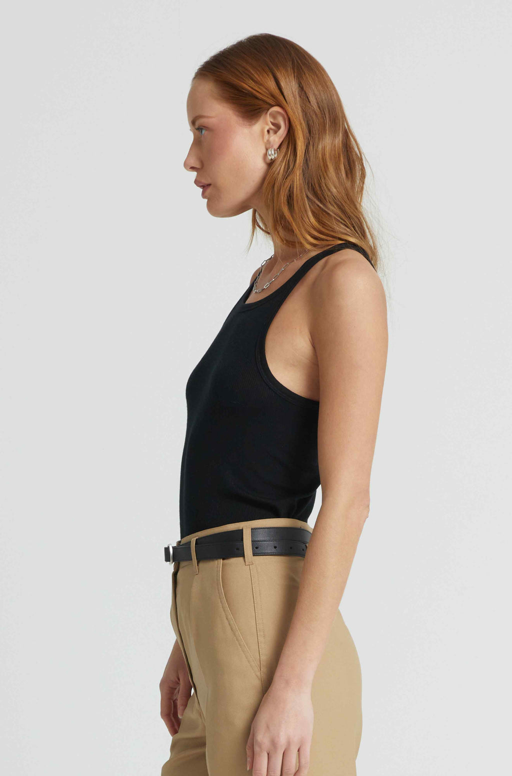 Woman wearing a black tank top and beige pants on a white background