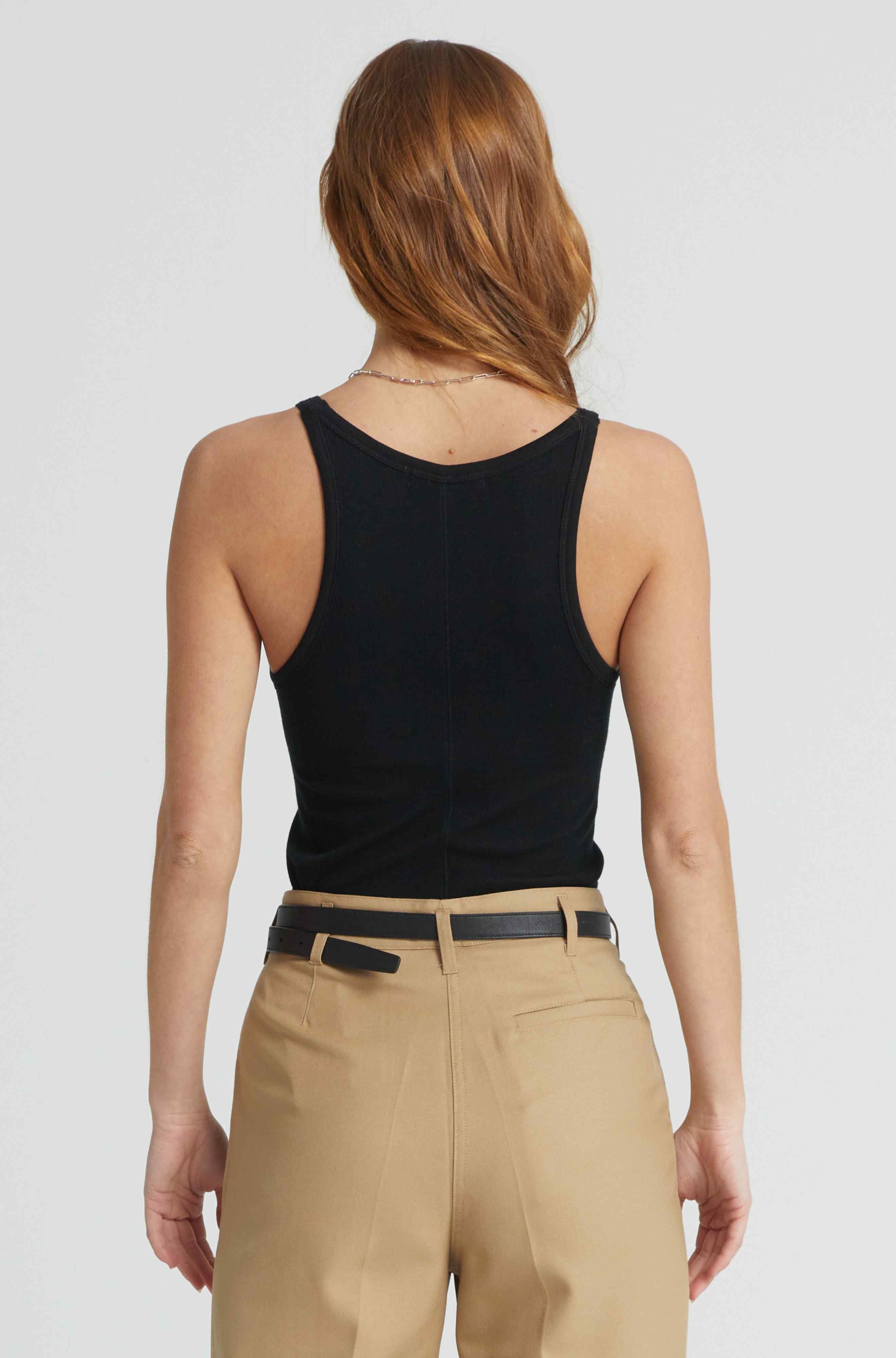 Person wearing a black tank top and beige pants on a plain background