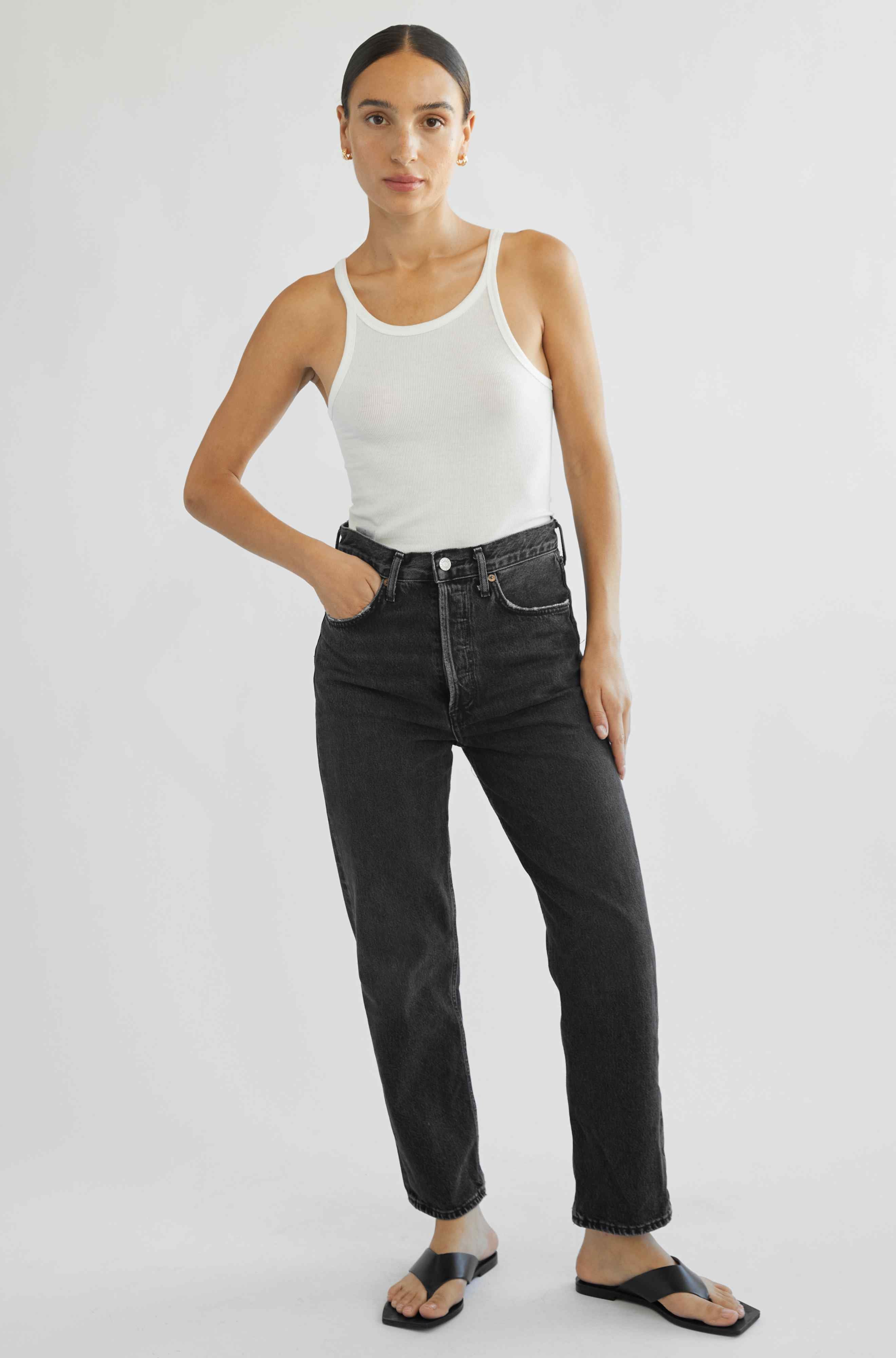 Woman wearing a white tank top and black jeans on a white background