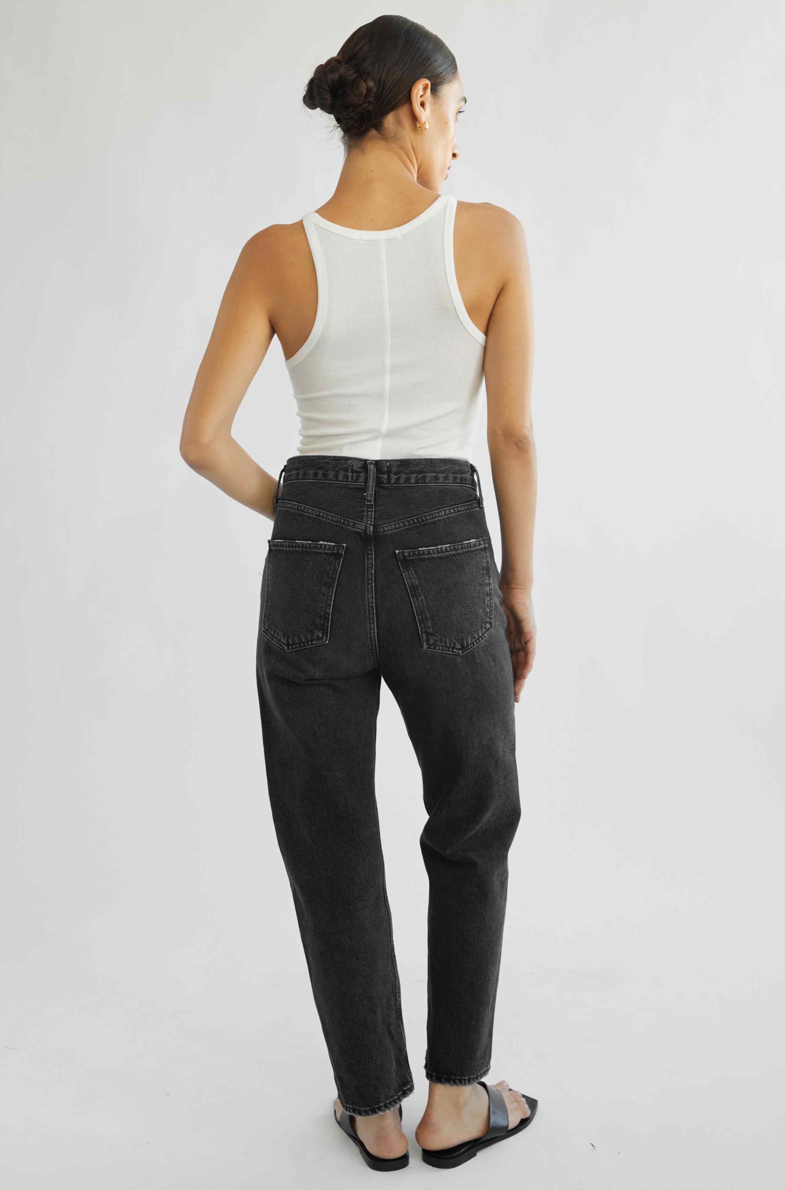 Person wearing a white sleeveless top and black jeans on a plain background