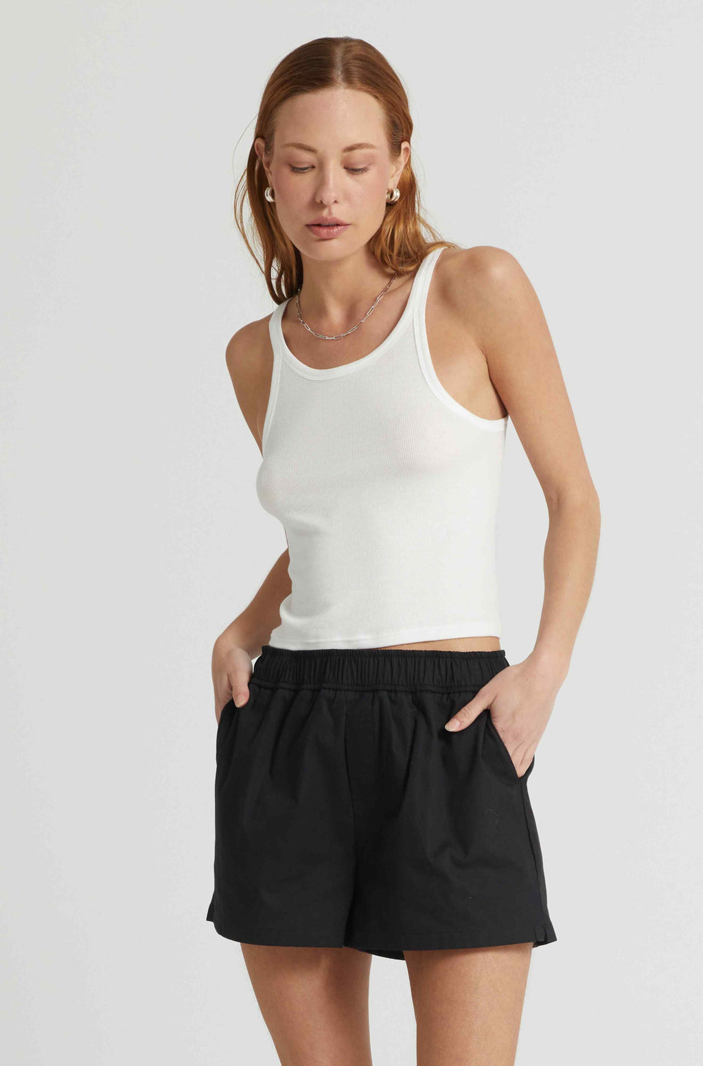 Woman wearing a white tank top and black shorts on a light gray background