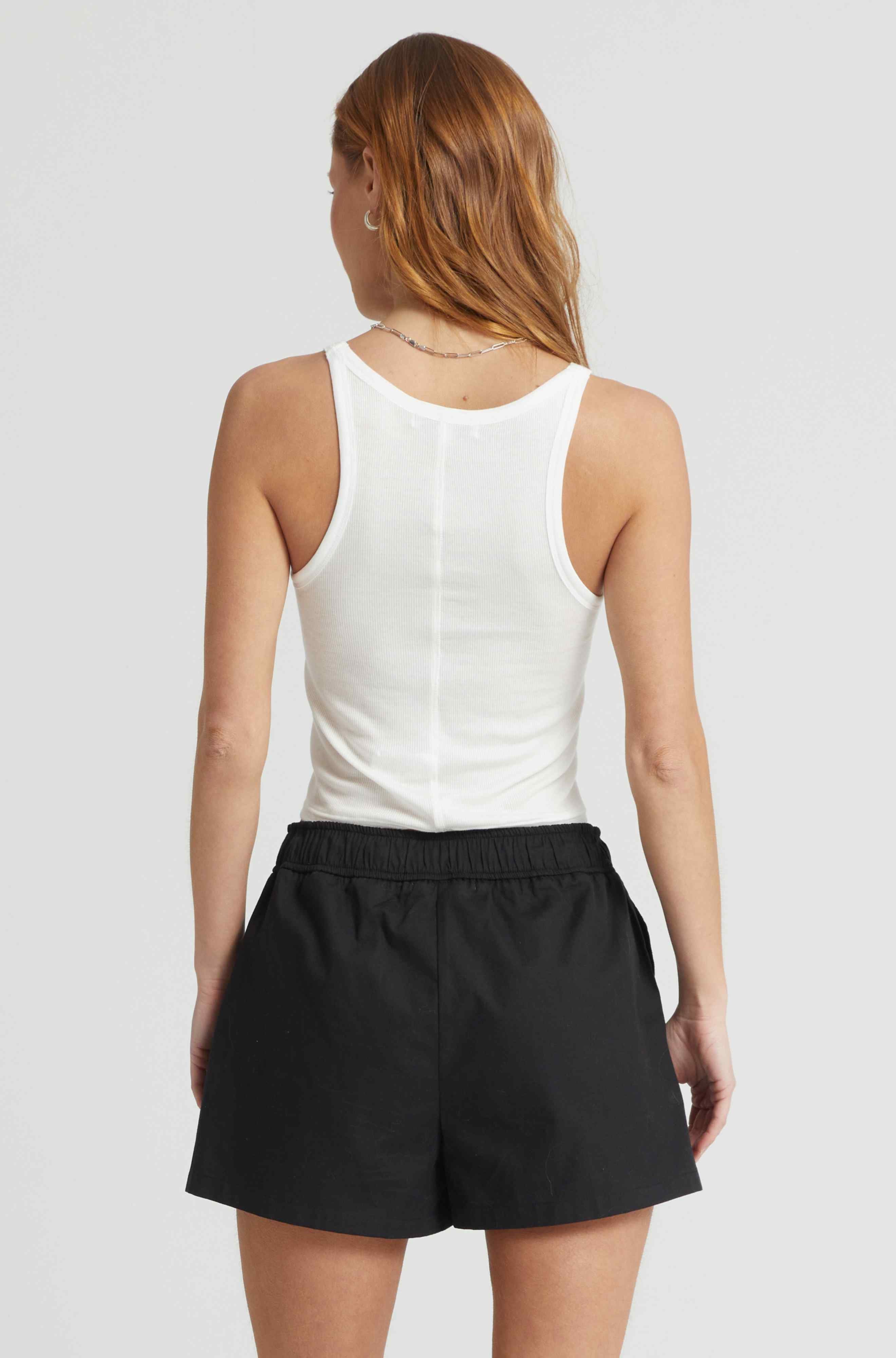 Woman wearing a white tank top and black shorts on a plain background