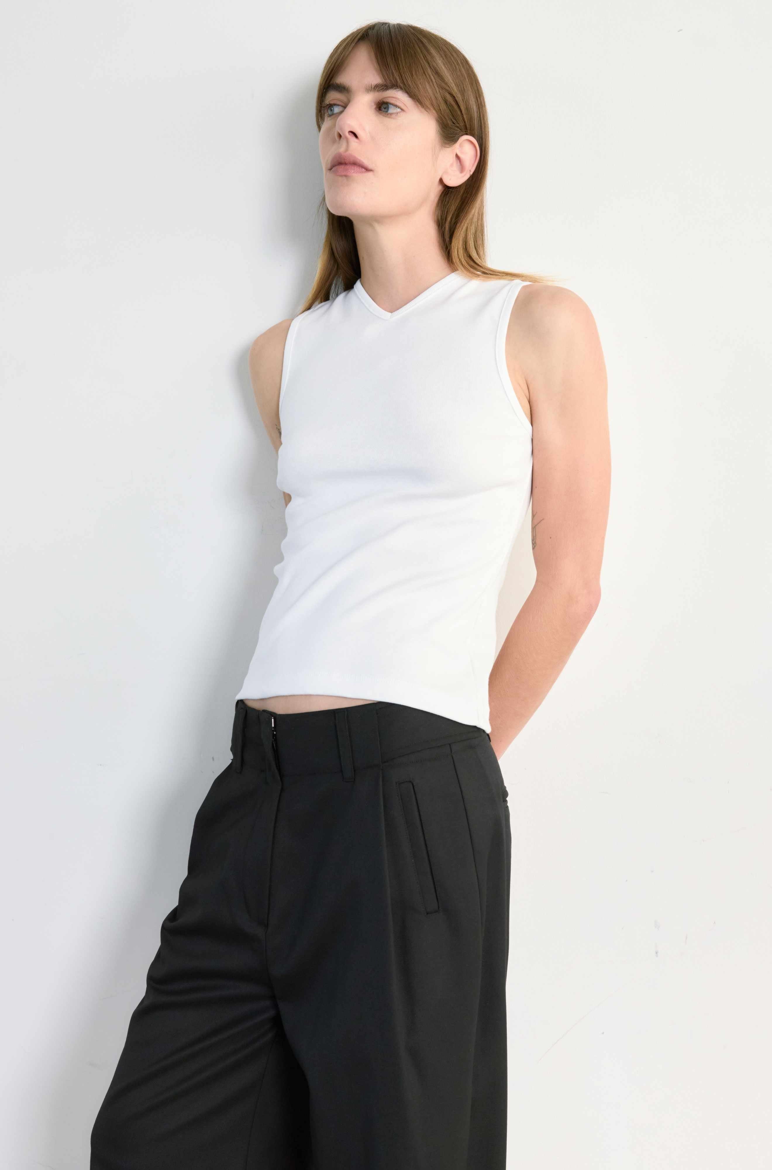 Woman wearing a white sleeveless top and black pants against a light gray background