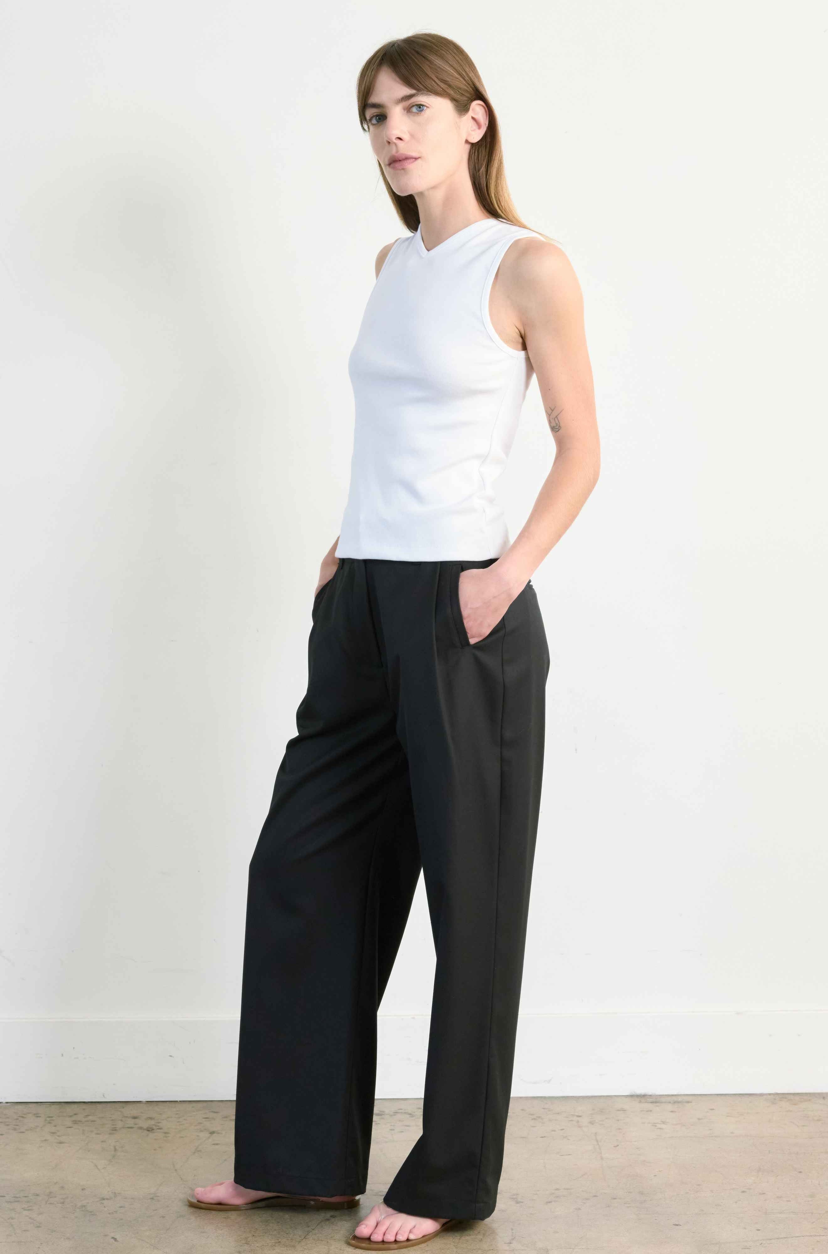 Woman wearing a white sleeveless top and black wide-leg pants against a plain background