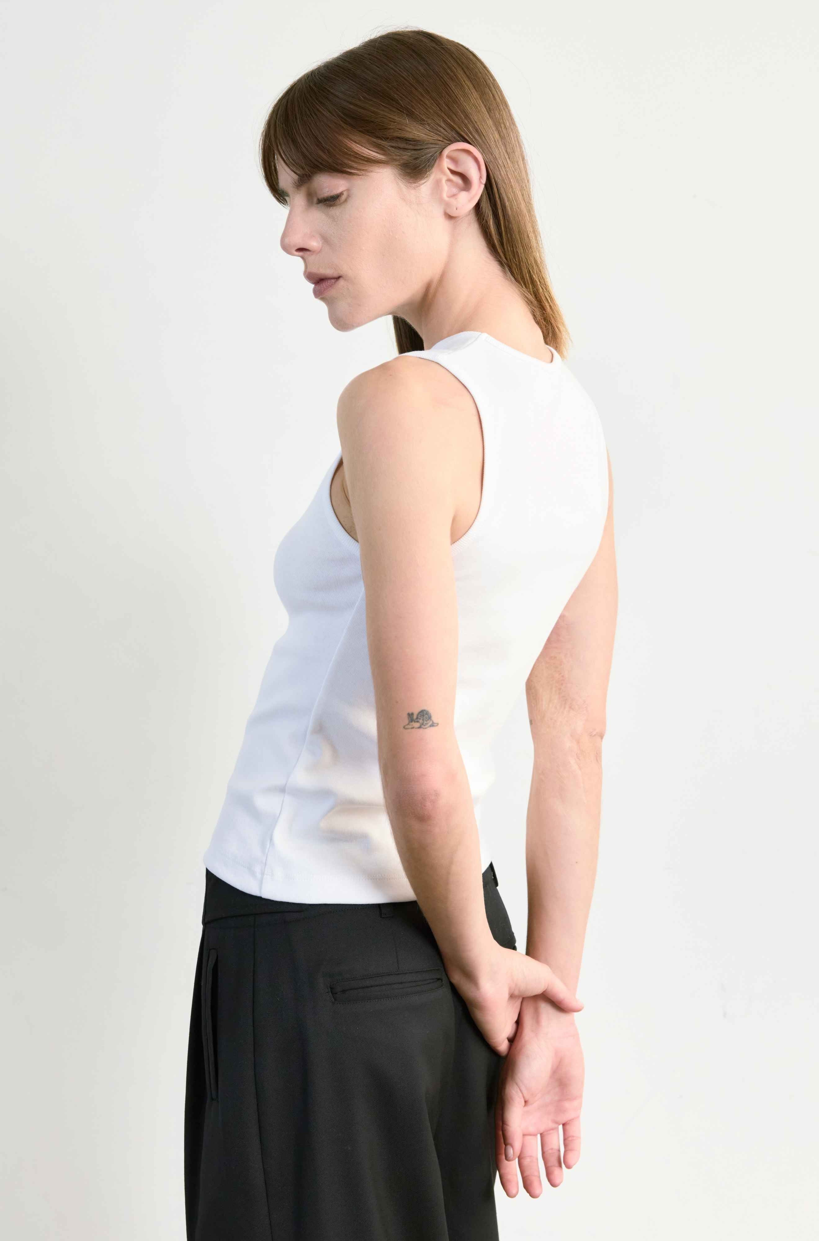 Woman wearing a white sleeveless top and black pants on a plain background