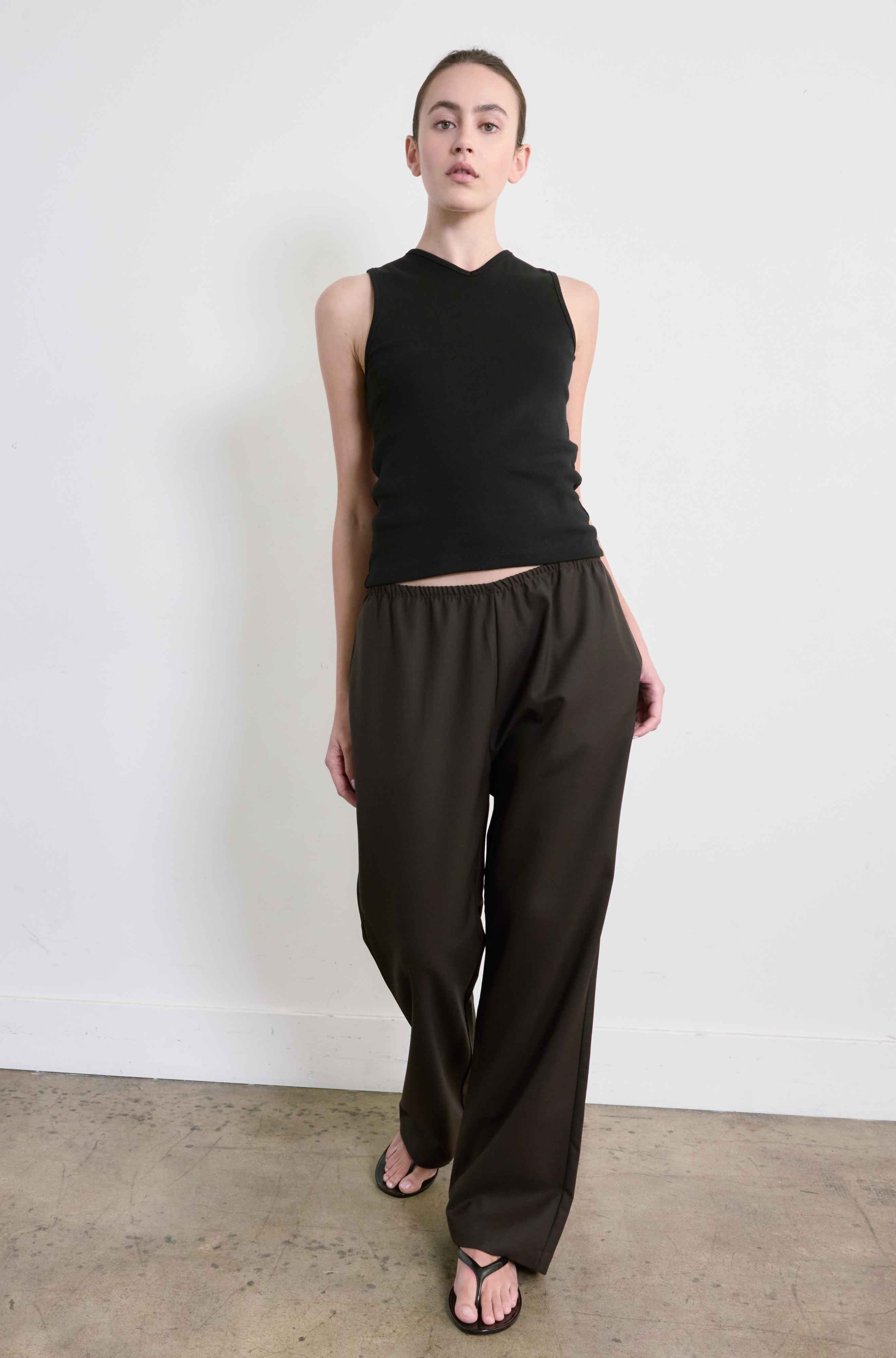 Person wearing a black sleeveless top and dark pants against a white background