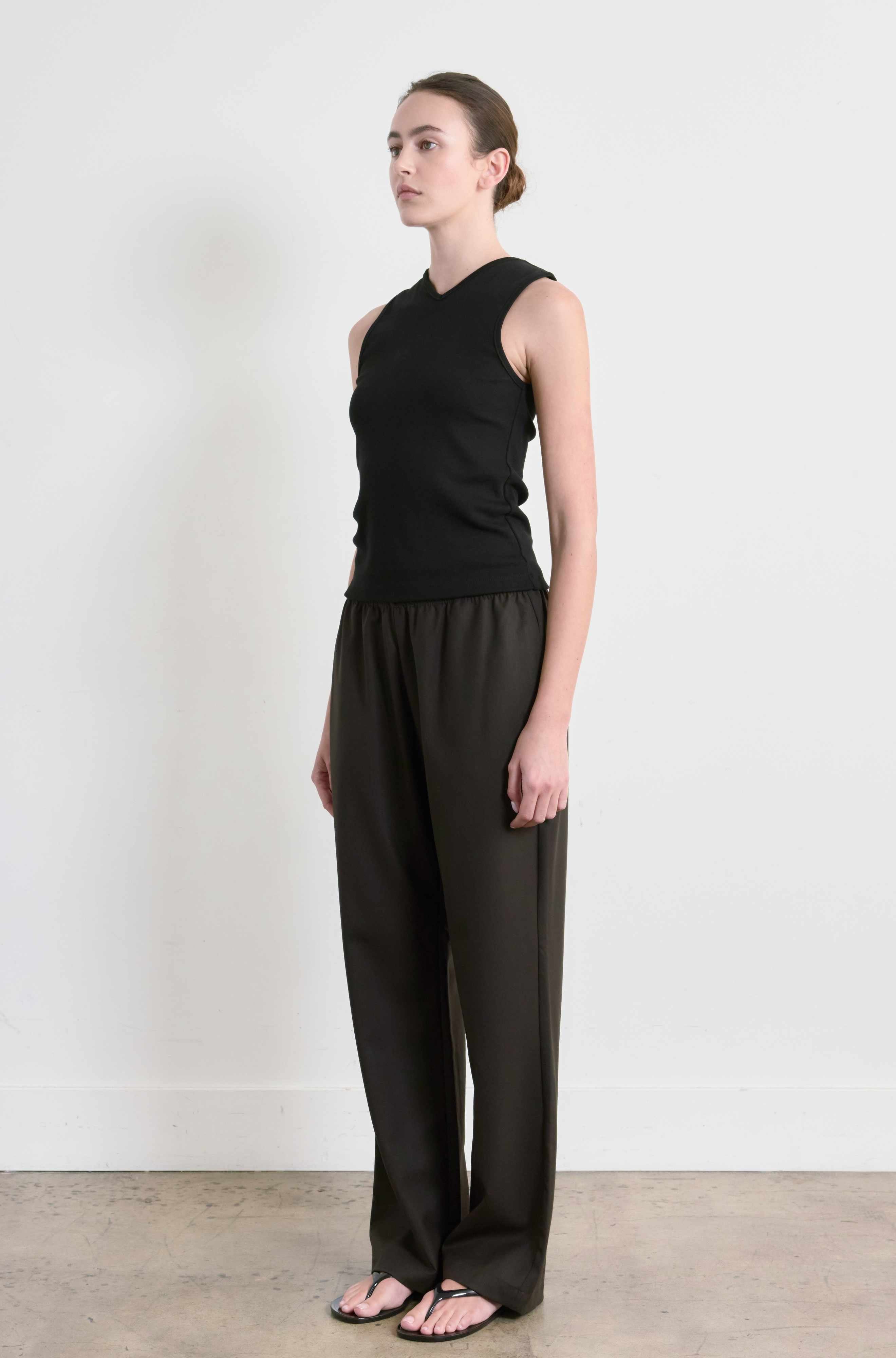 Woman wearing a black sleeveless top and wide-leg pants against a white background