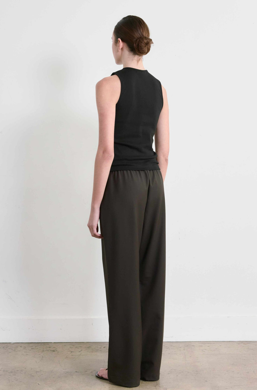 Woman wearing a black sleeveless top and dark pants against a white background