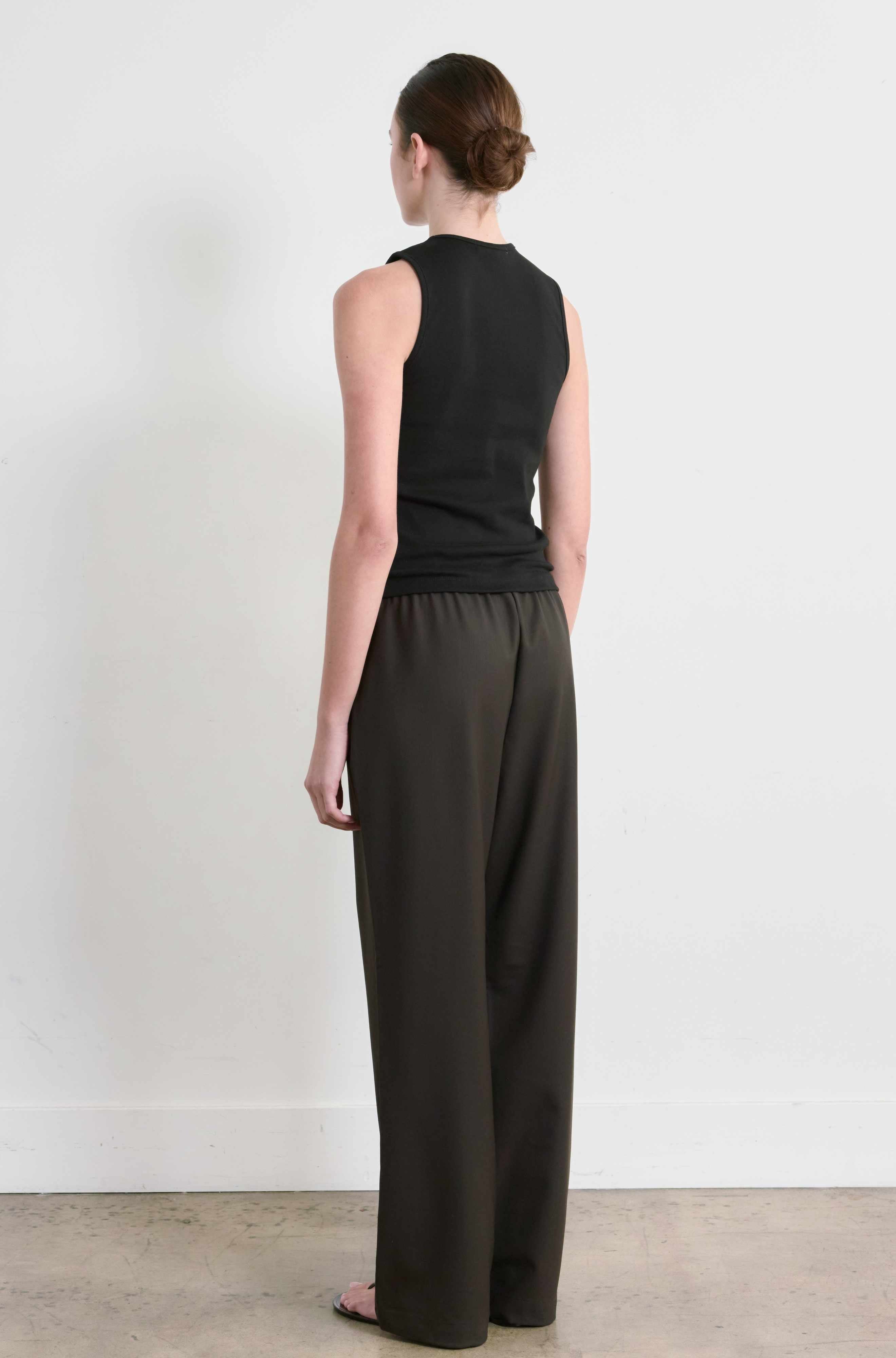 Woman wearing a black sleeveless top and dark pants against a white background