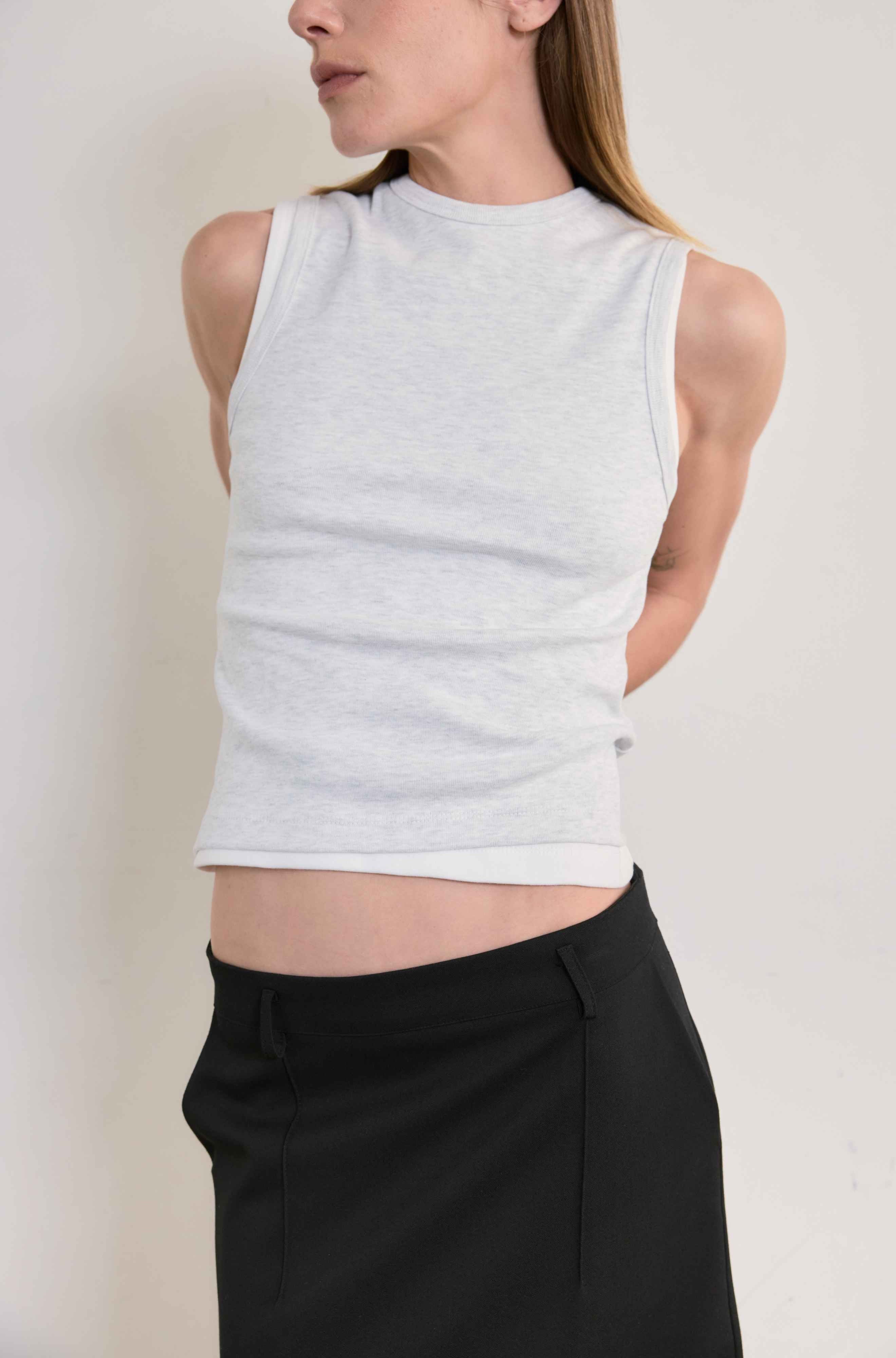 Person wearing a grey sleeveless top and black pants against a plain background