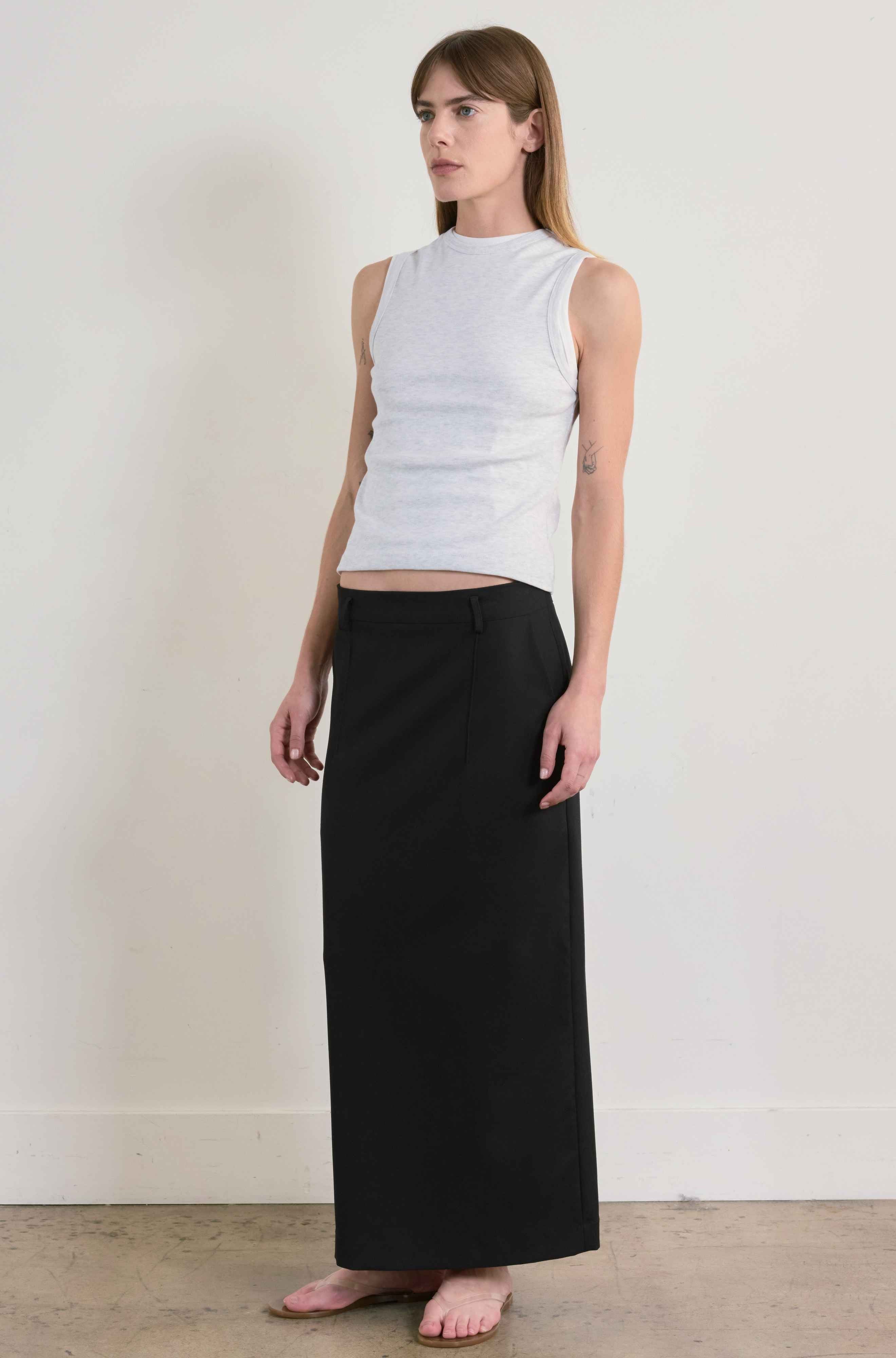 Woman wearing a grey sleeveless top and black skirt against a plain background