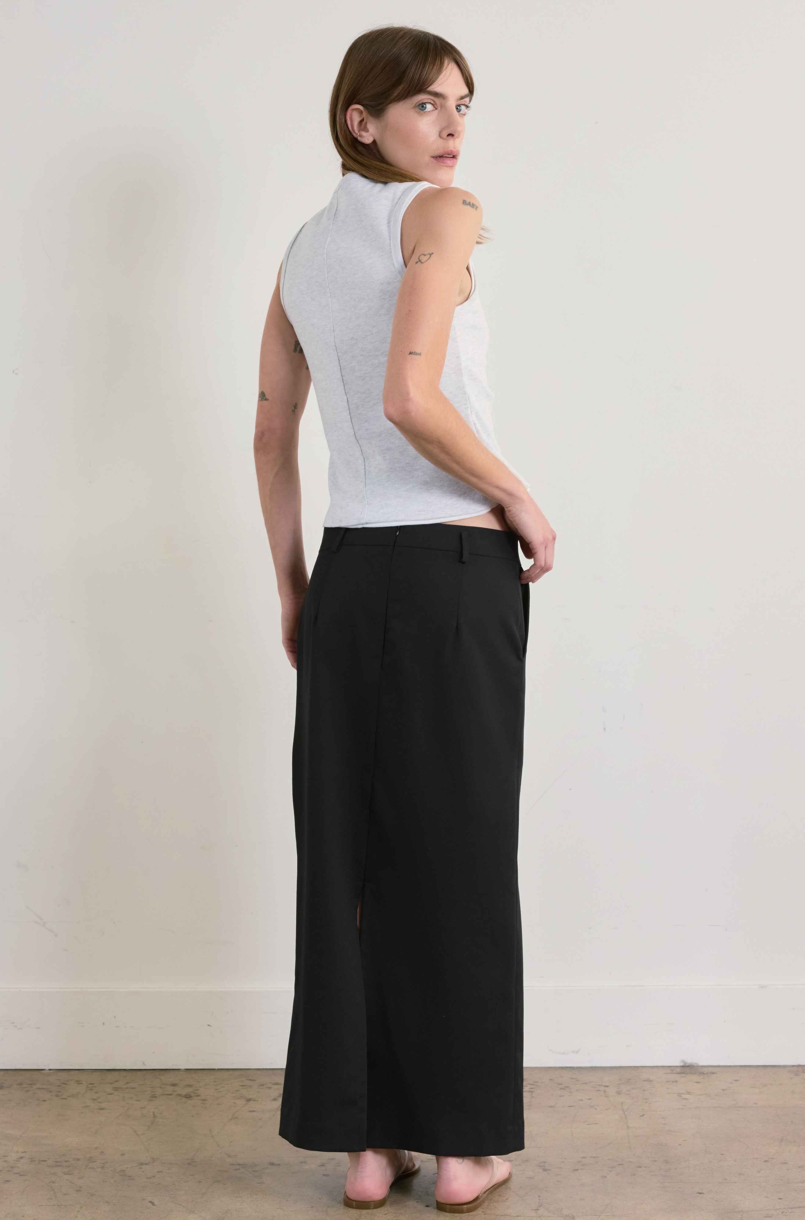 Woman wearing a grey sleeveless top and black pants against a plain background