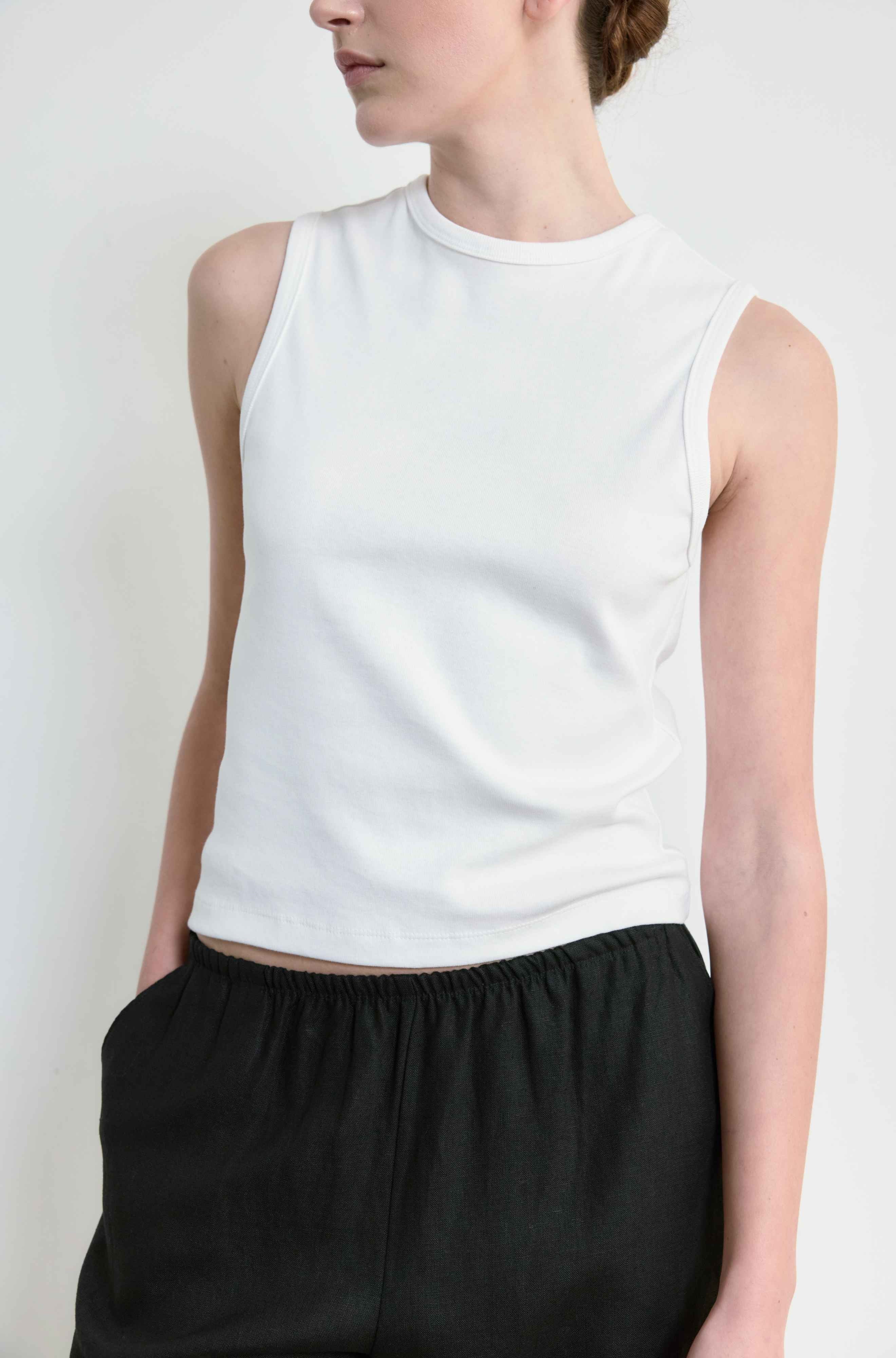 Person wearing a white sleeveless top and black pants against a plain background
