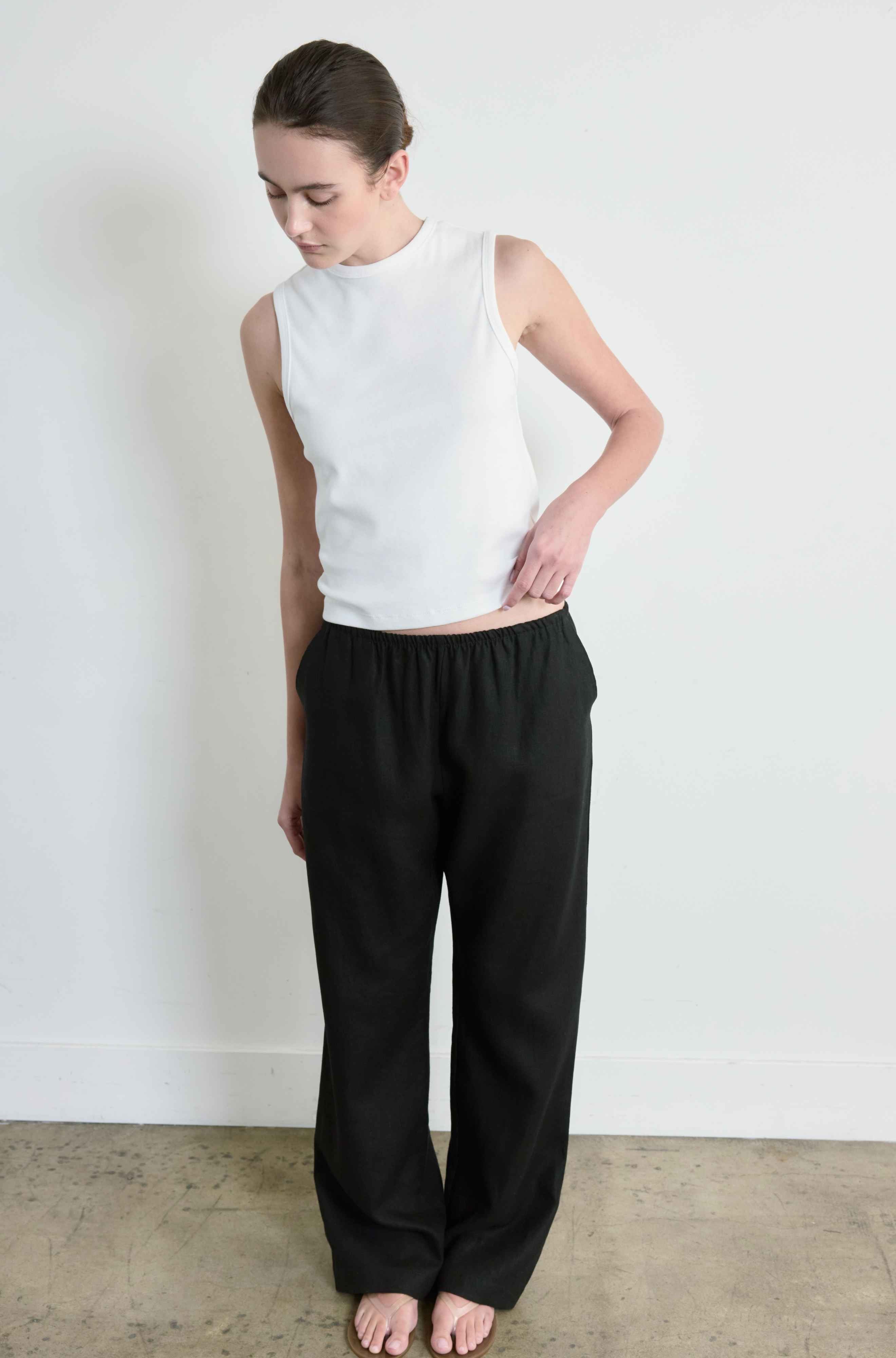 Person wearing a white sleeveless top and black pants against a plain background