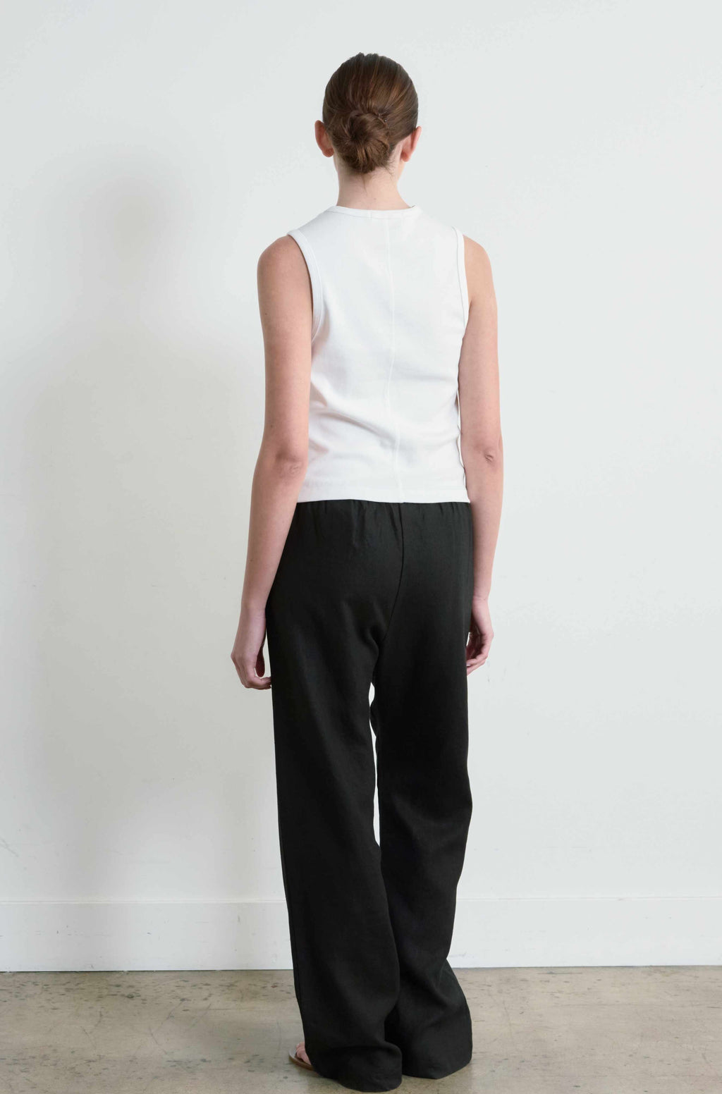 Person wearing a white sleeveless top and black pants against a plain white background