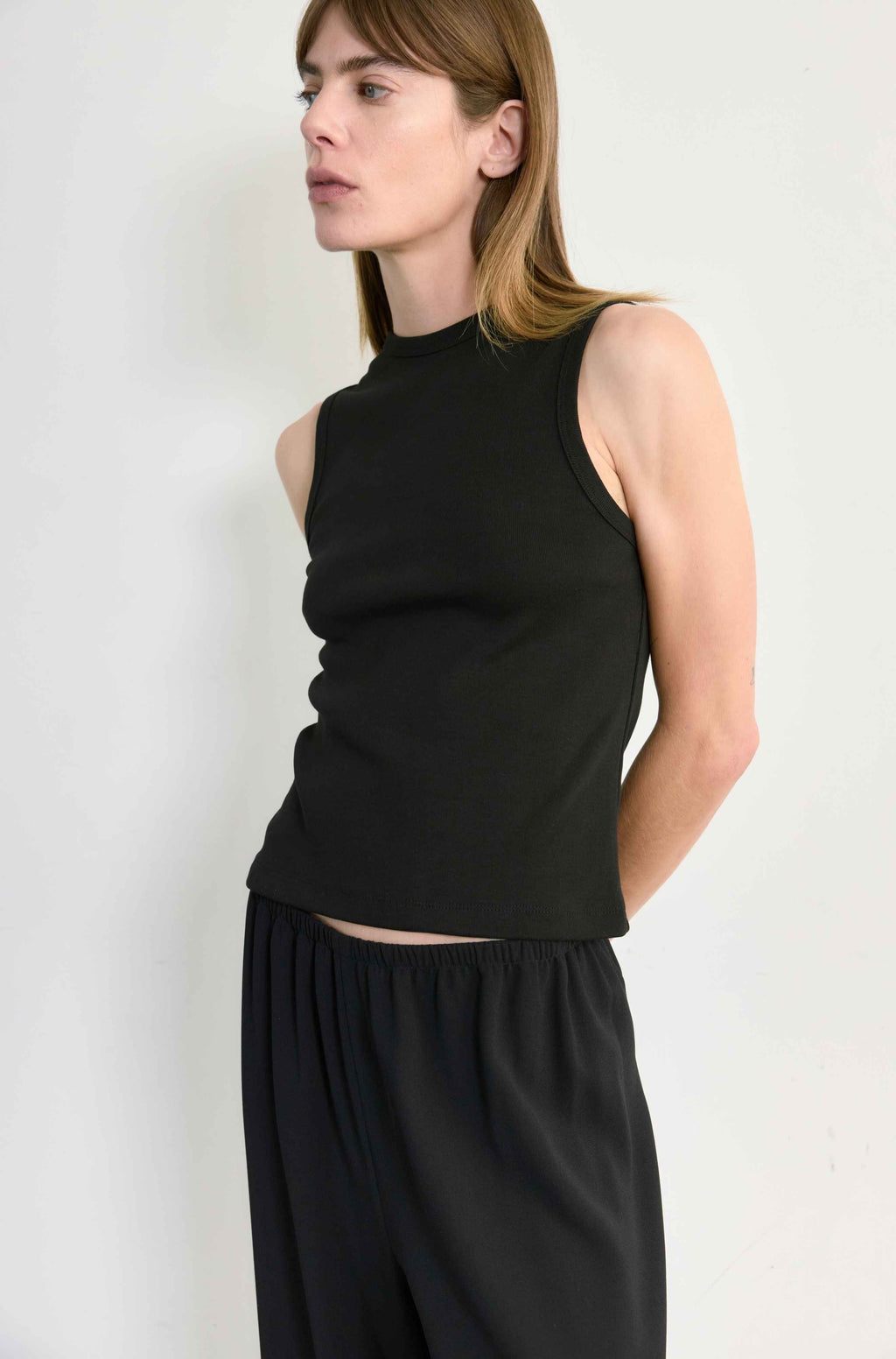 Woman wearing a black sleeveless top and black pants against a white background
