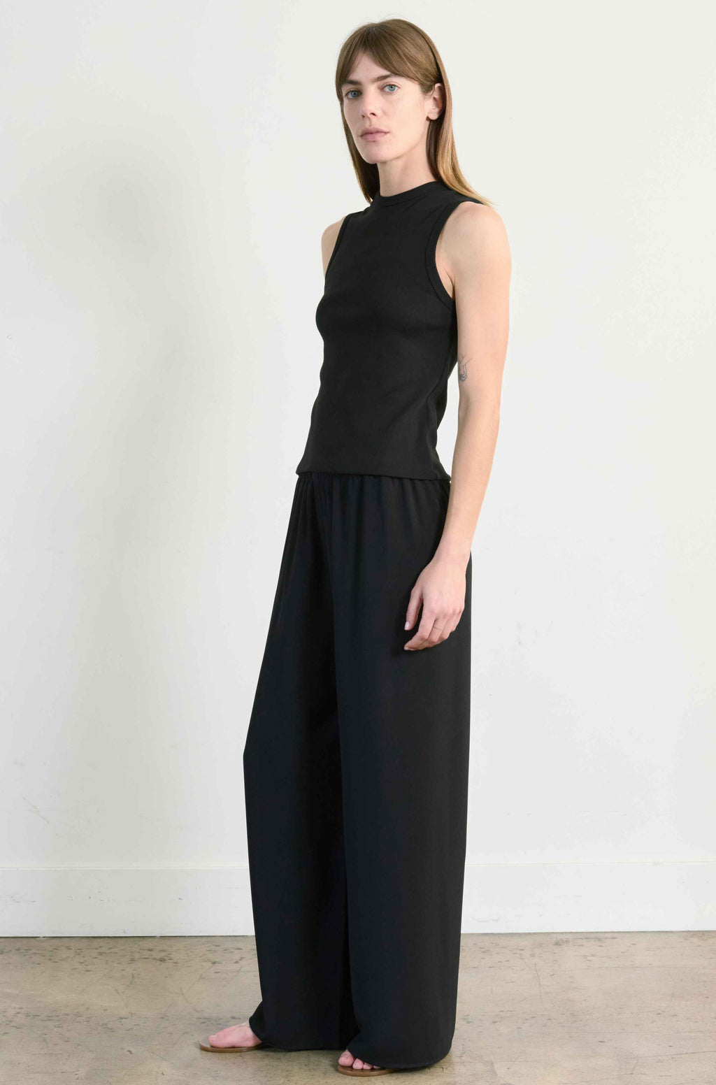 Woman wearing a black sleeveless top and wide-leg pants against a white background