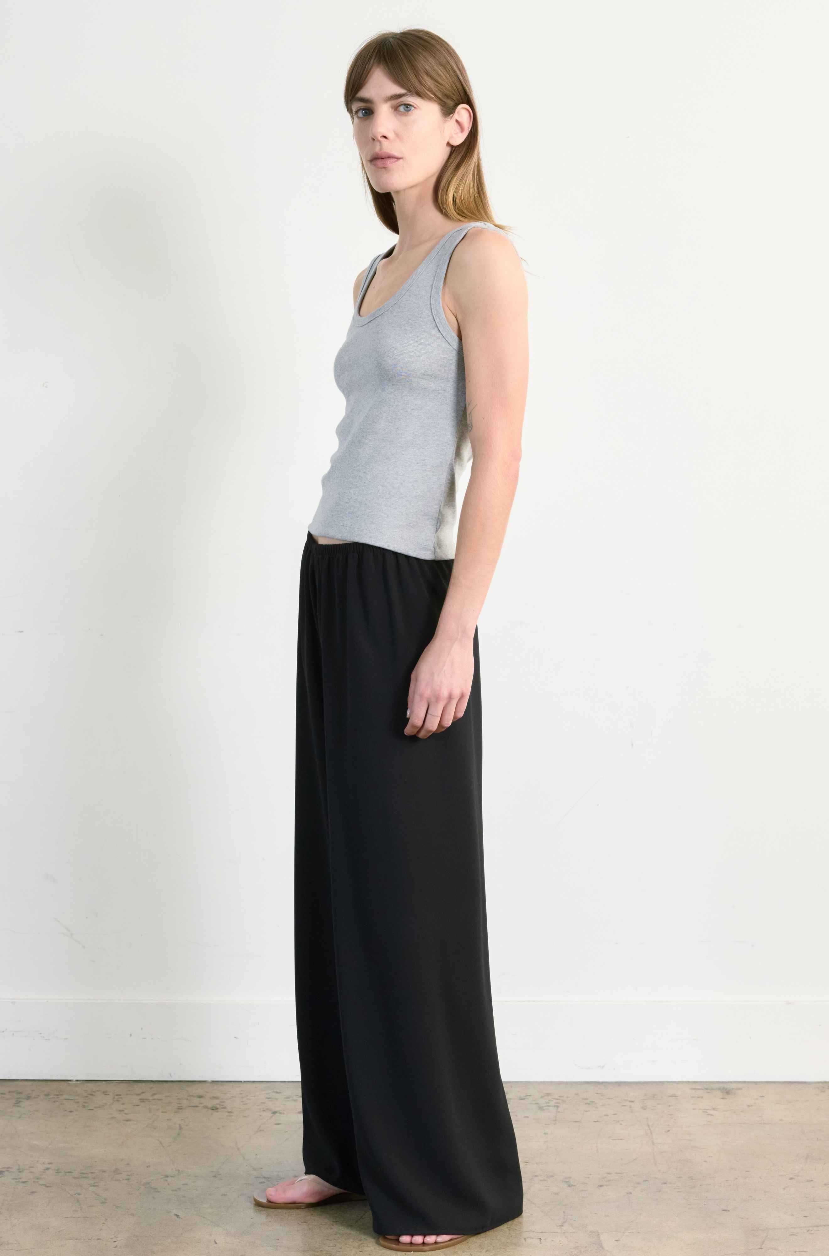 Woman wearing a gray sleeveless top and black flowing pants against a white background