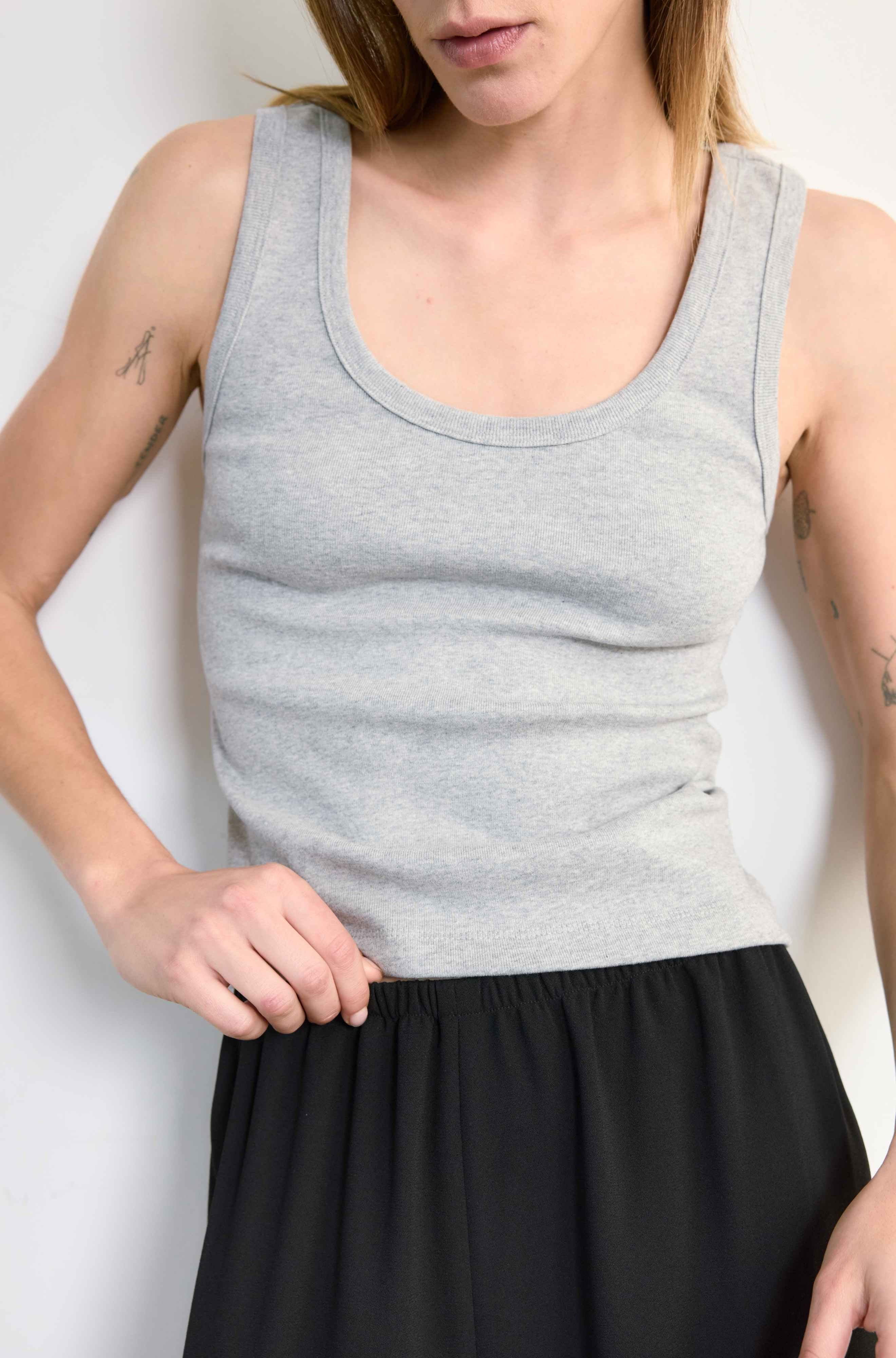 Person wearing a gray tank top and black skirt against a white background