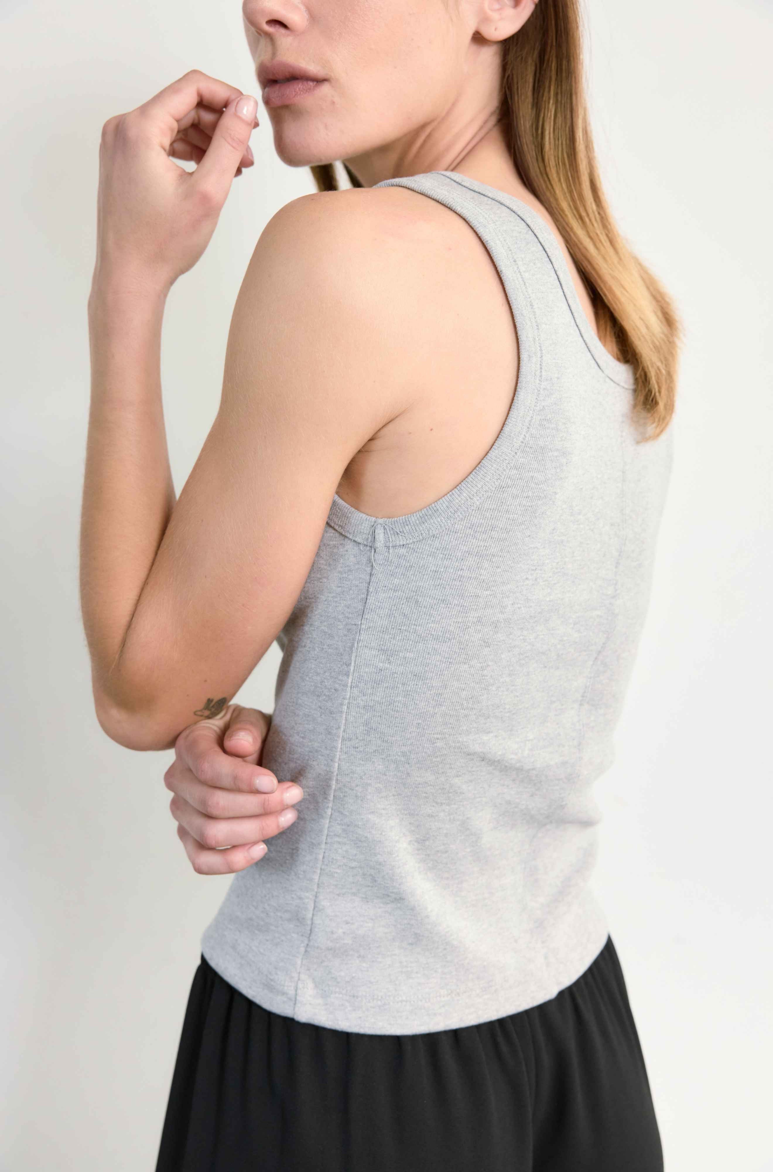 Woman wearing a light gray sleeveless top and black pants on a plain background