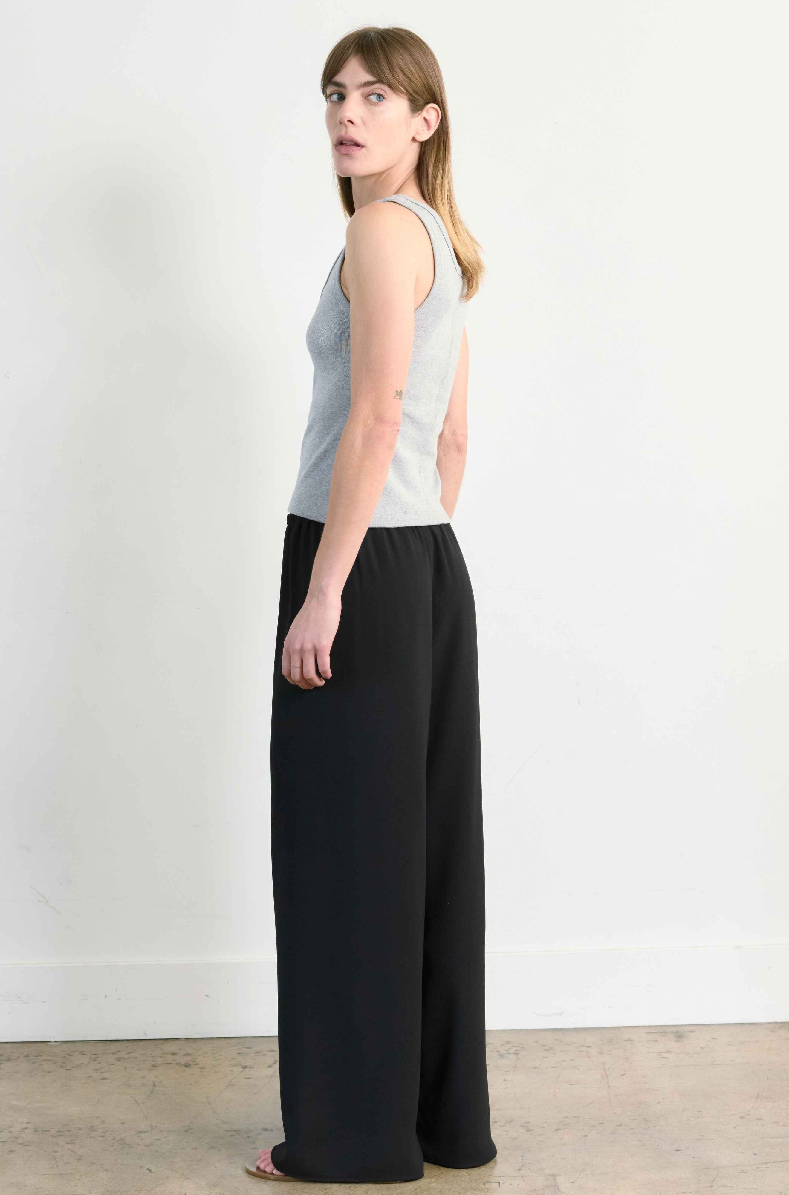 Woman wearing a gray sleeveless top and black wide-leg pants against a white background