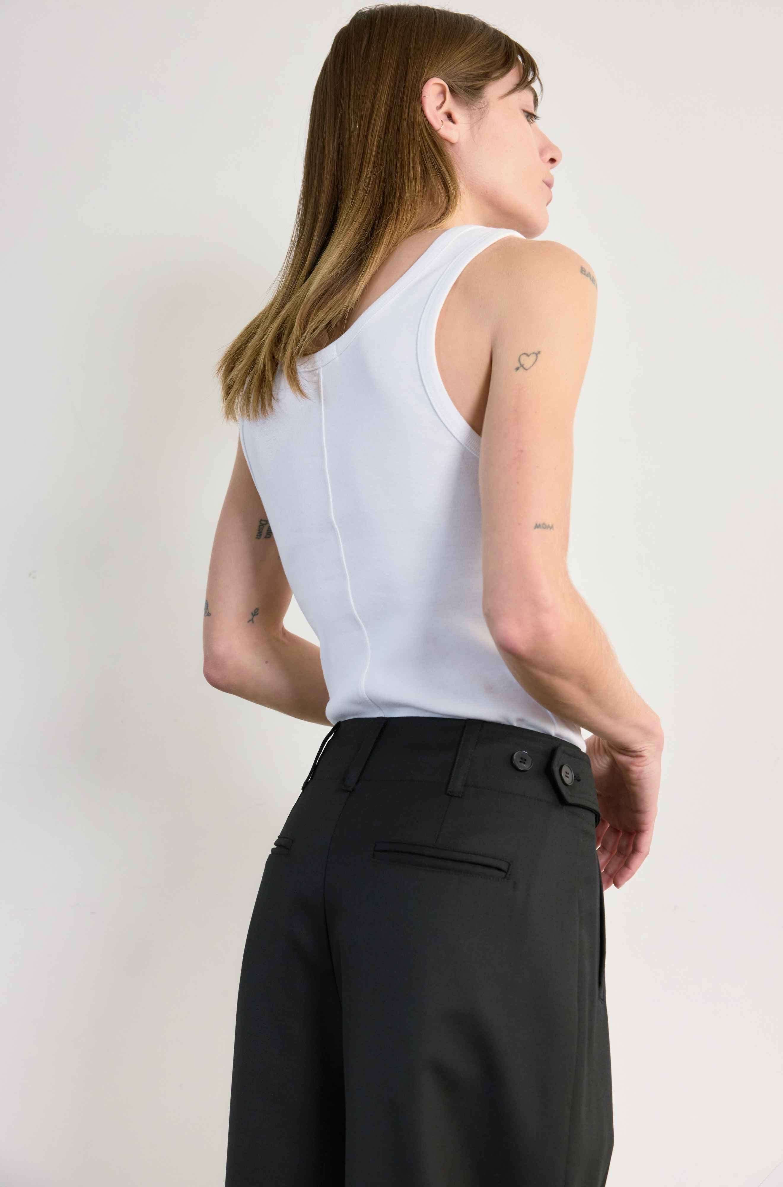 Woman wearing a white sleeveless top and black pants against a plain background