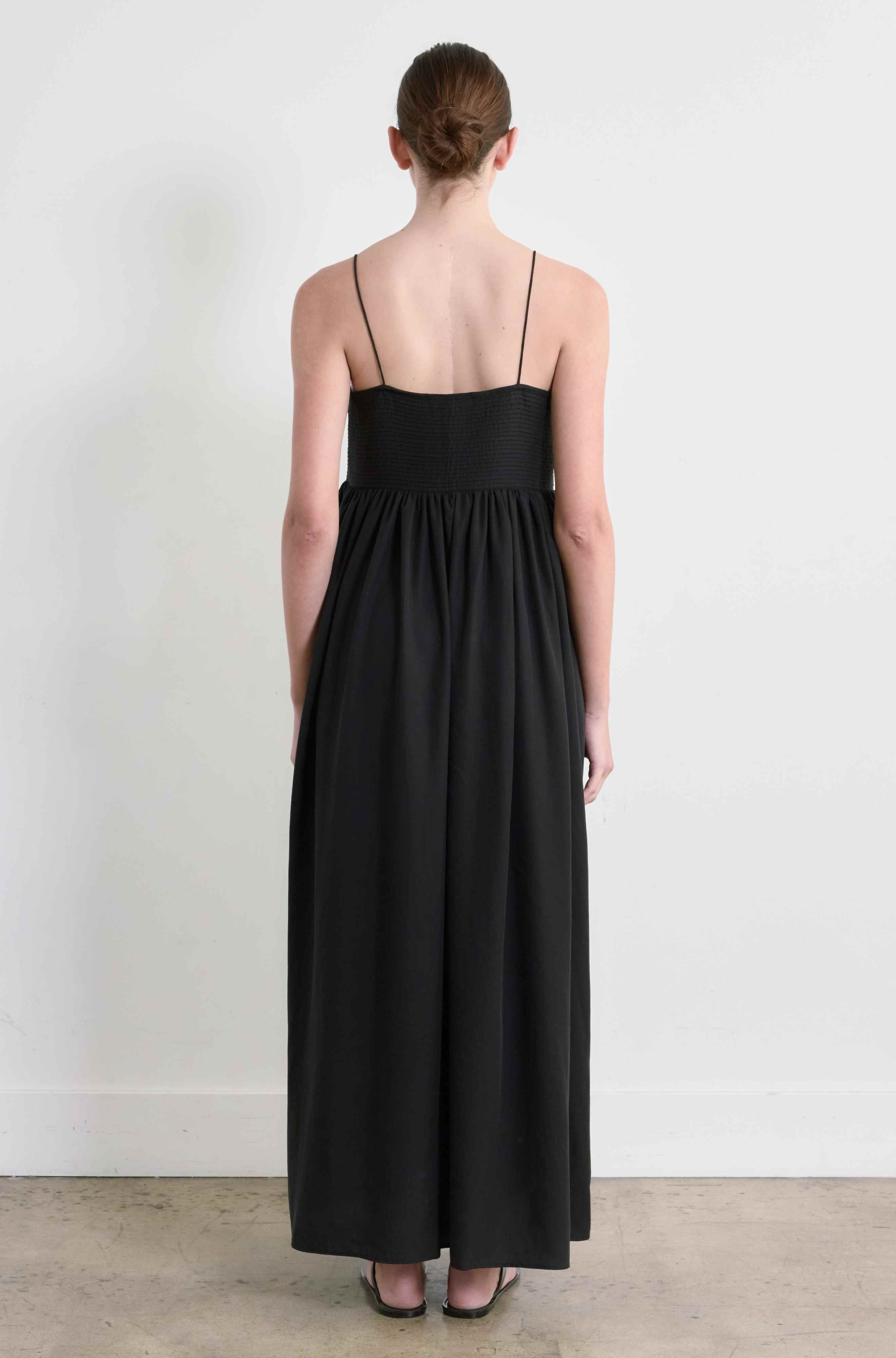 Person wearing a black dress standing against a white wall.