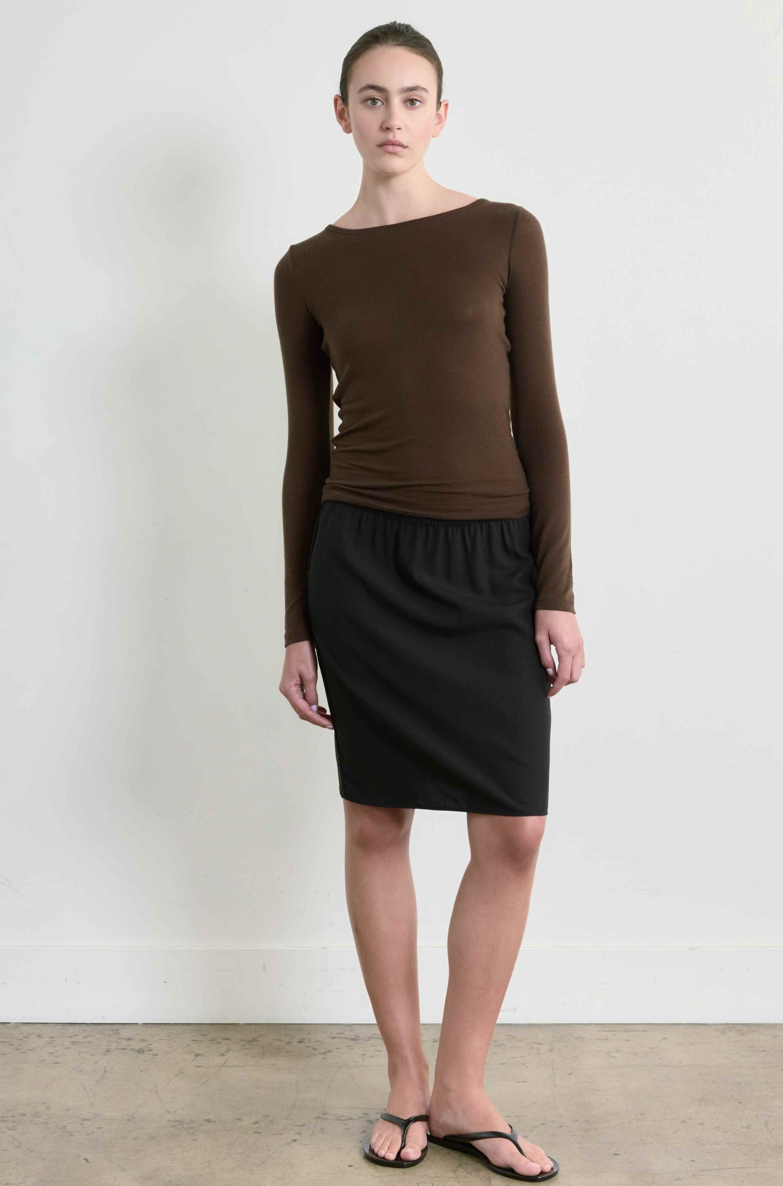 Woman wearing a brown long-sleeve top and black skirt against a white background