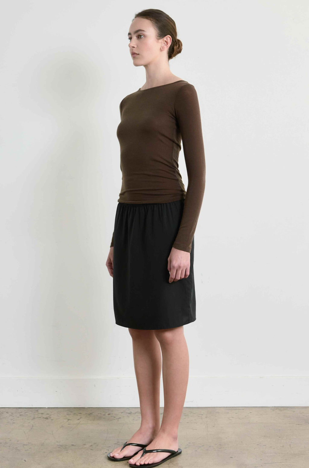 Woman wearing a brown long-sleeve top and black skirt against a white background