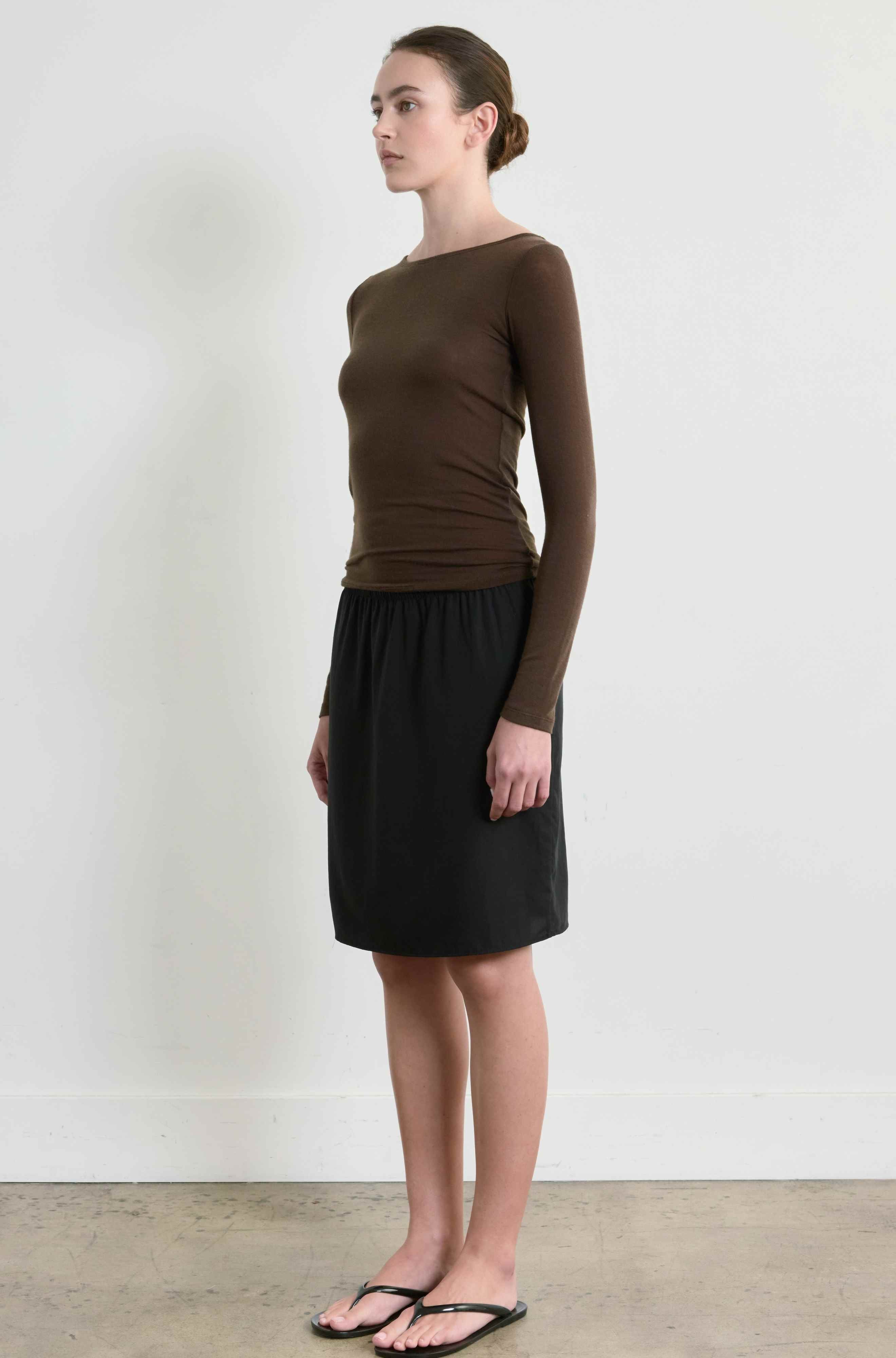 Woman wearing a brown long-sleeve top and black skirt against a white background