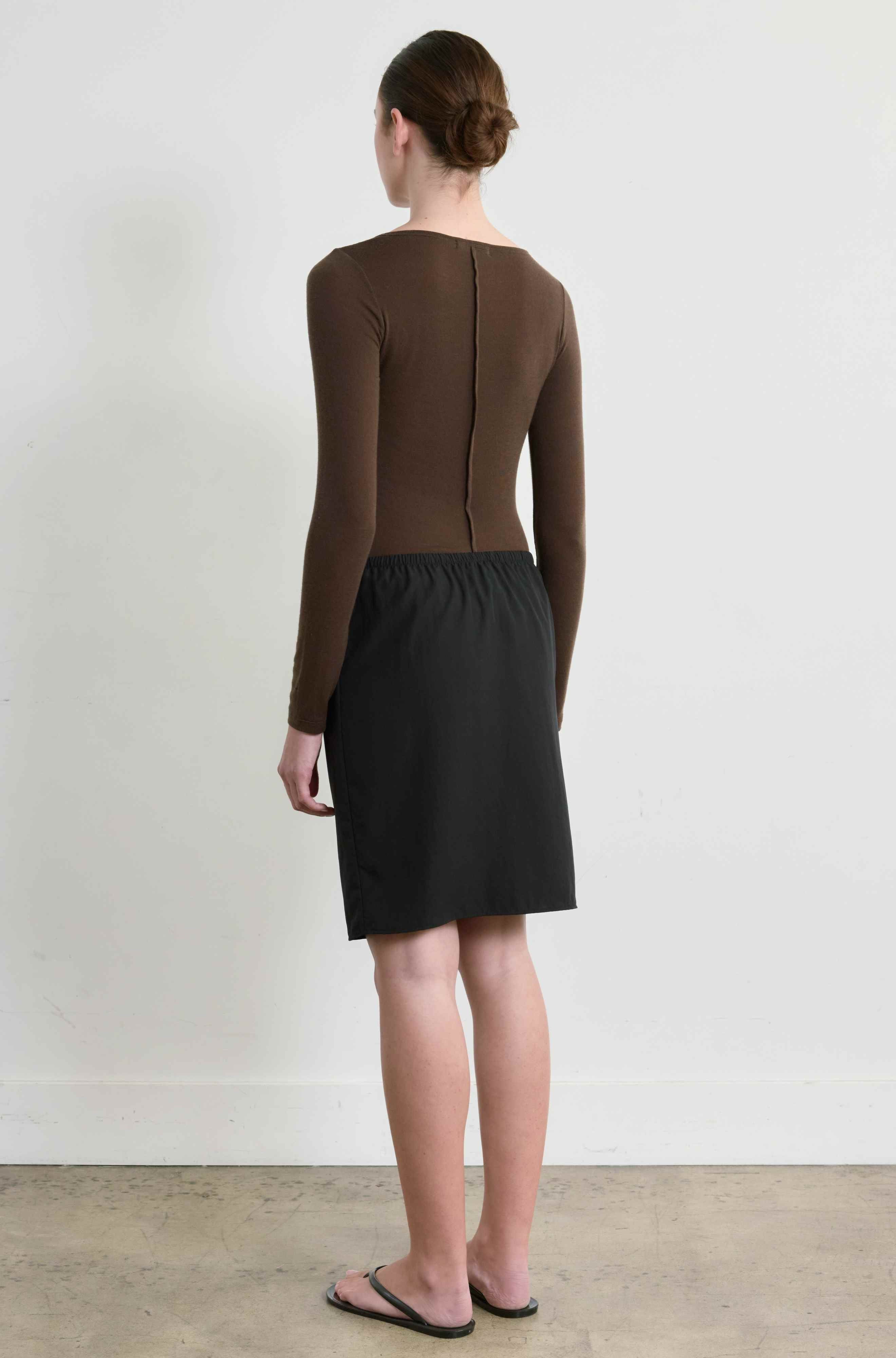 Person wearing a brown long-sleeve top and black skirt against a white background