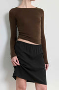 Person wearing a brown long-sleeve top and black skirt on a white background