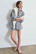 Woman wearing a checkered outfit with a white sweater draped over her shoulders against a plain background