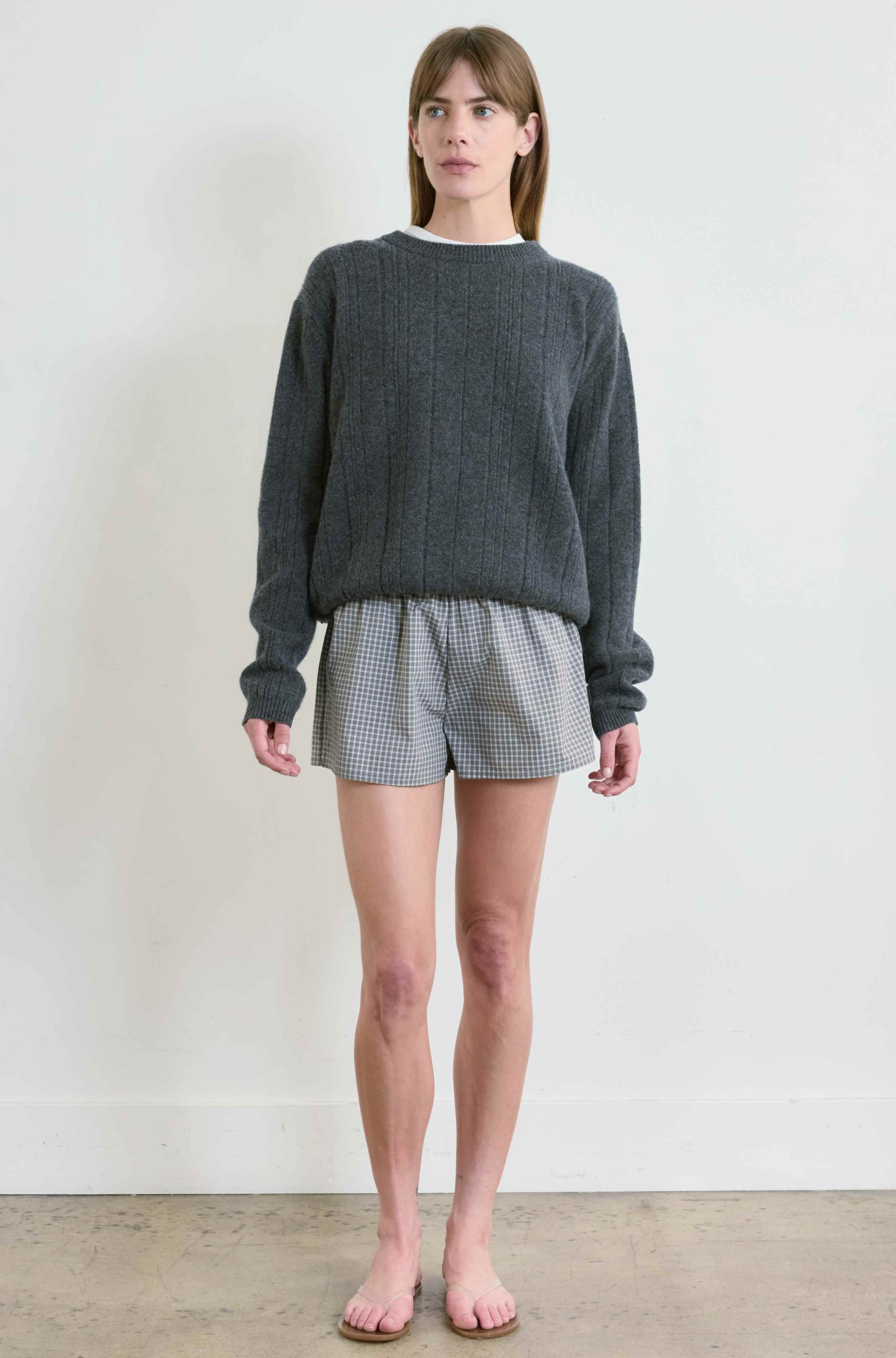Woman wearing a dark gray sweater and checkered shorts against a white background