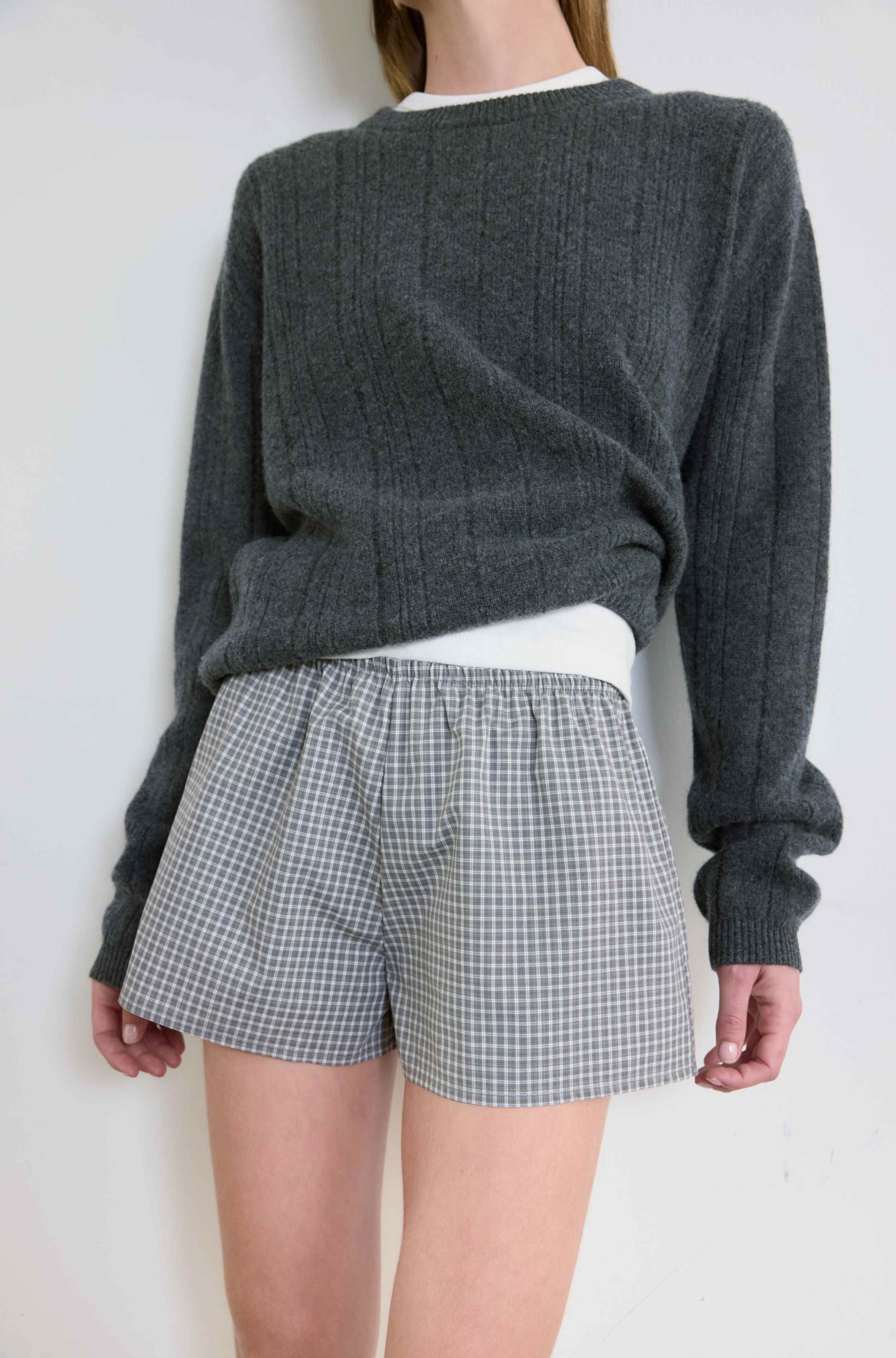 Person wearing a gray sweater and checkered shorts against a white background