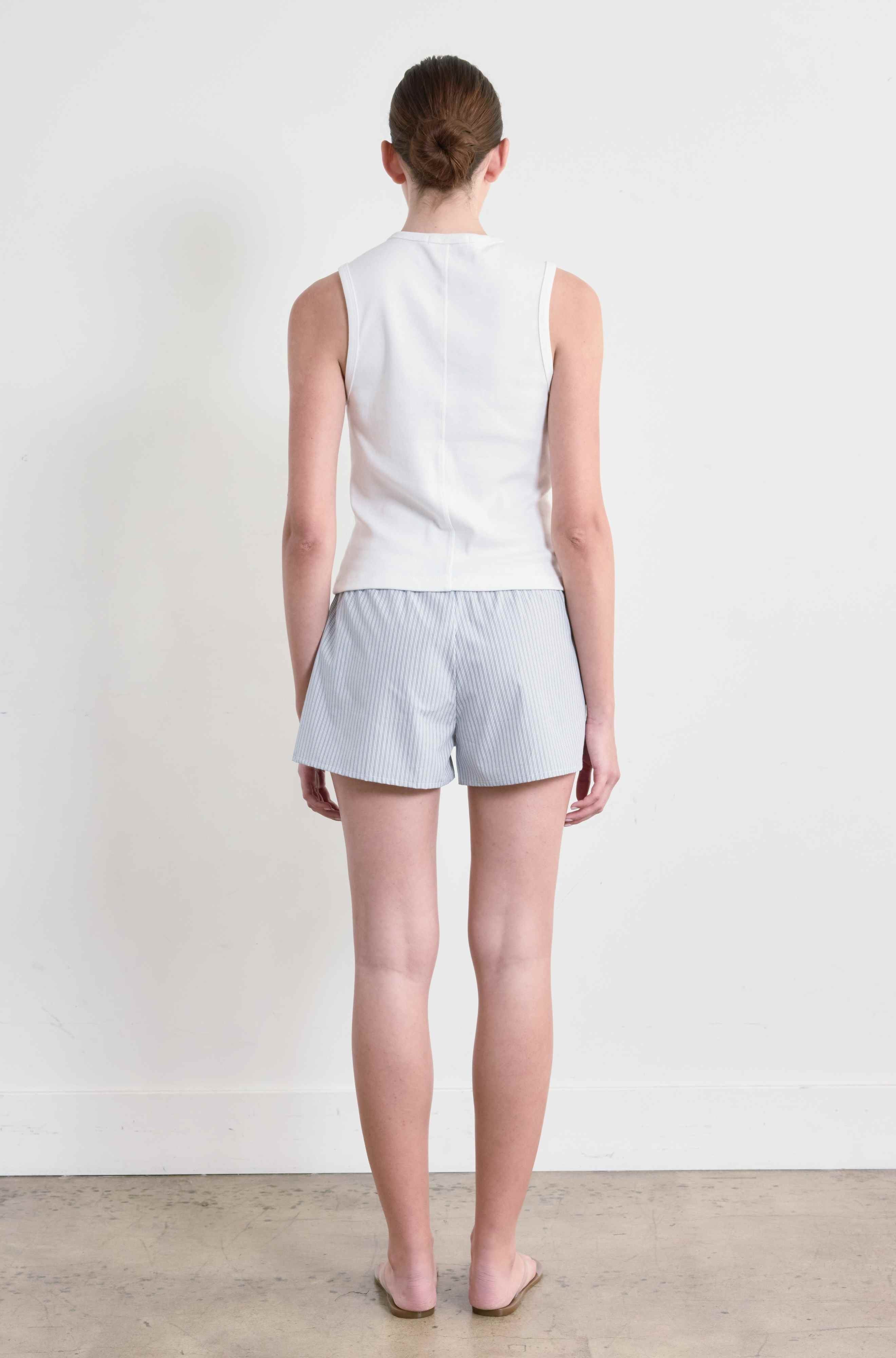 Person wearing a white sleeveless top and light gray shorts against a plain white background