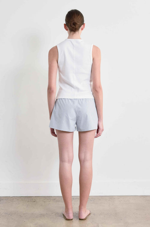 Person wearing a white sleeveless top and light gray shorts against a plain white background
