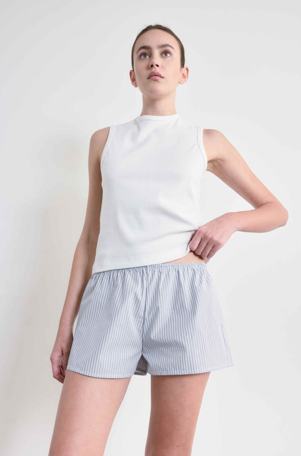 Woman wearing a white sleeveless top and striped shorts on a plain background
